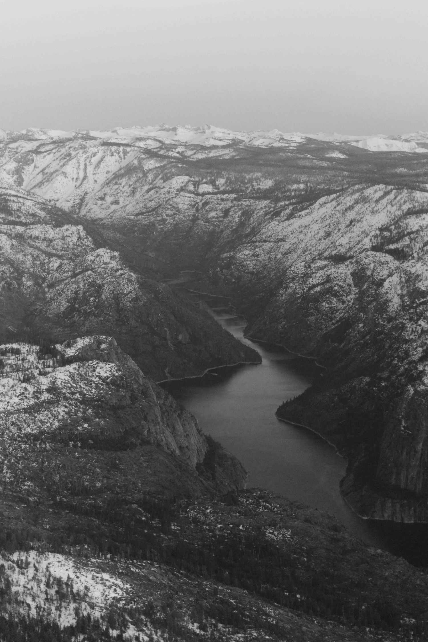 b+w photo of hetch hetchy reservoir surrounded by snowcapped mountains, as seen from the sky