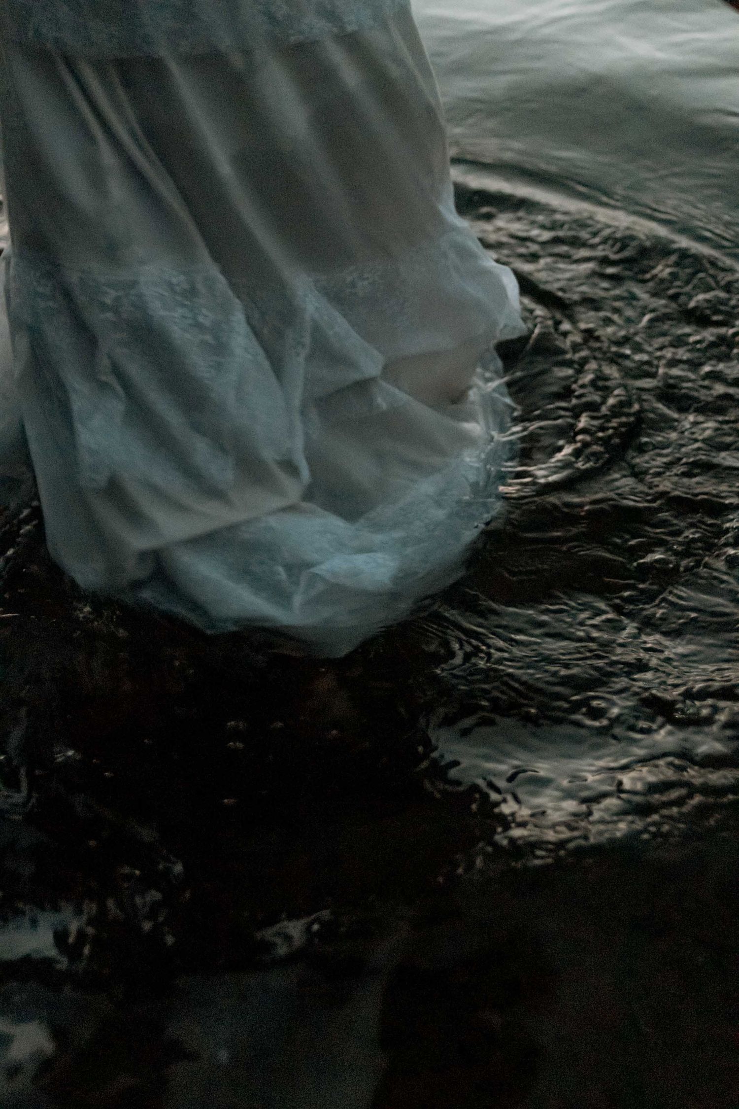 close up of person in white dress wading in water at twilight