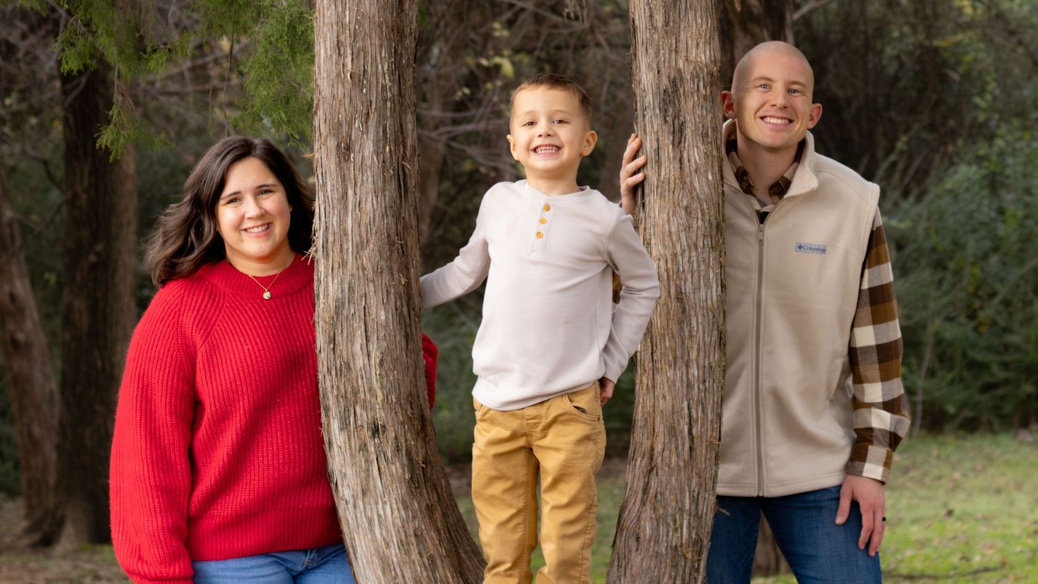 DFW family photography session with parents and young child smiling outdoors among trees during a relaxed portrait session.