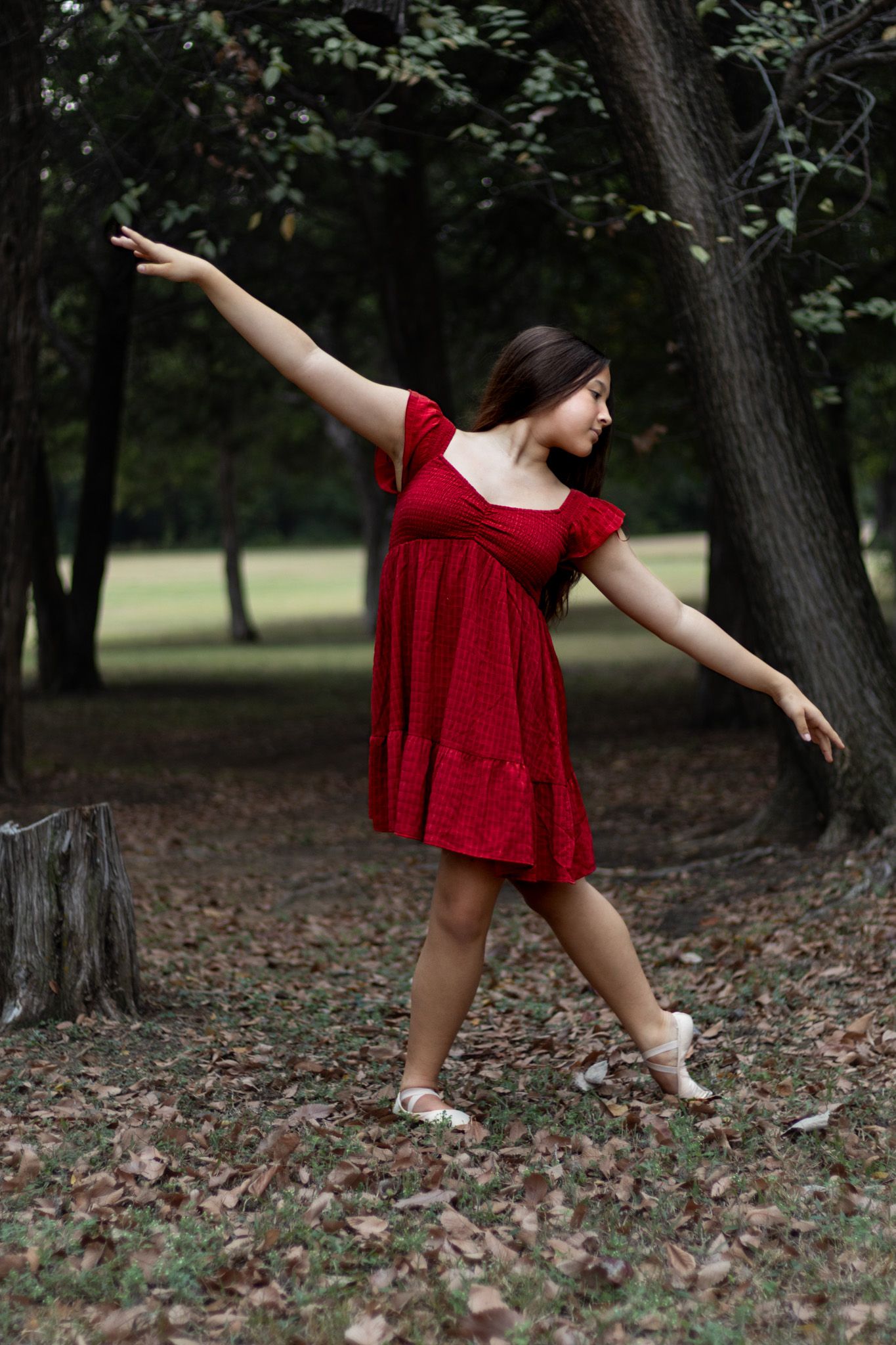 young woman in red dress outdoor portrait photography with graceful dance pose among trees natural light elegant expressive portrait session