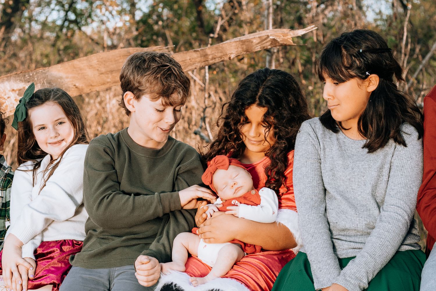 Family portrait of siblings sitting together outdoors with a newborn baby, captured in natural light during a relaxed lifestyle family photo