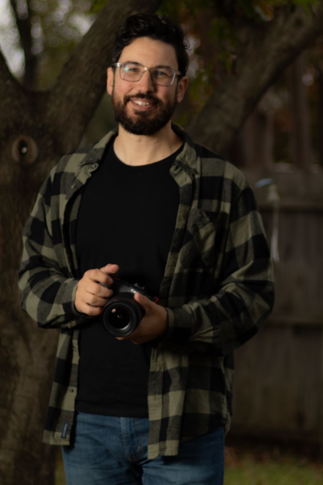 Smiling portrait photographer holding camera outdoors with blurred natural background, professional portrait photography