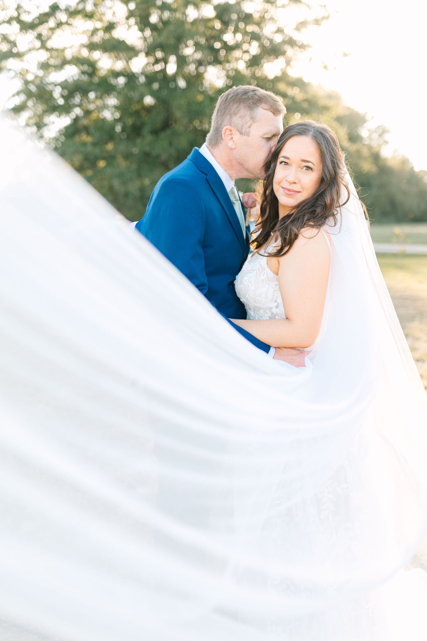 Dreamy wedding portrait with billowing veil in golden sunlight.