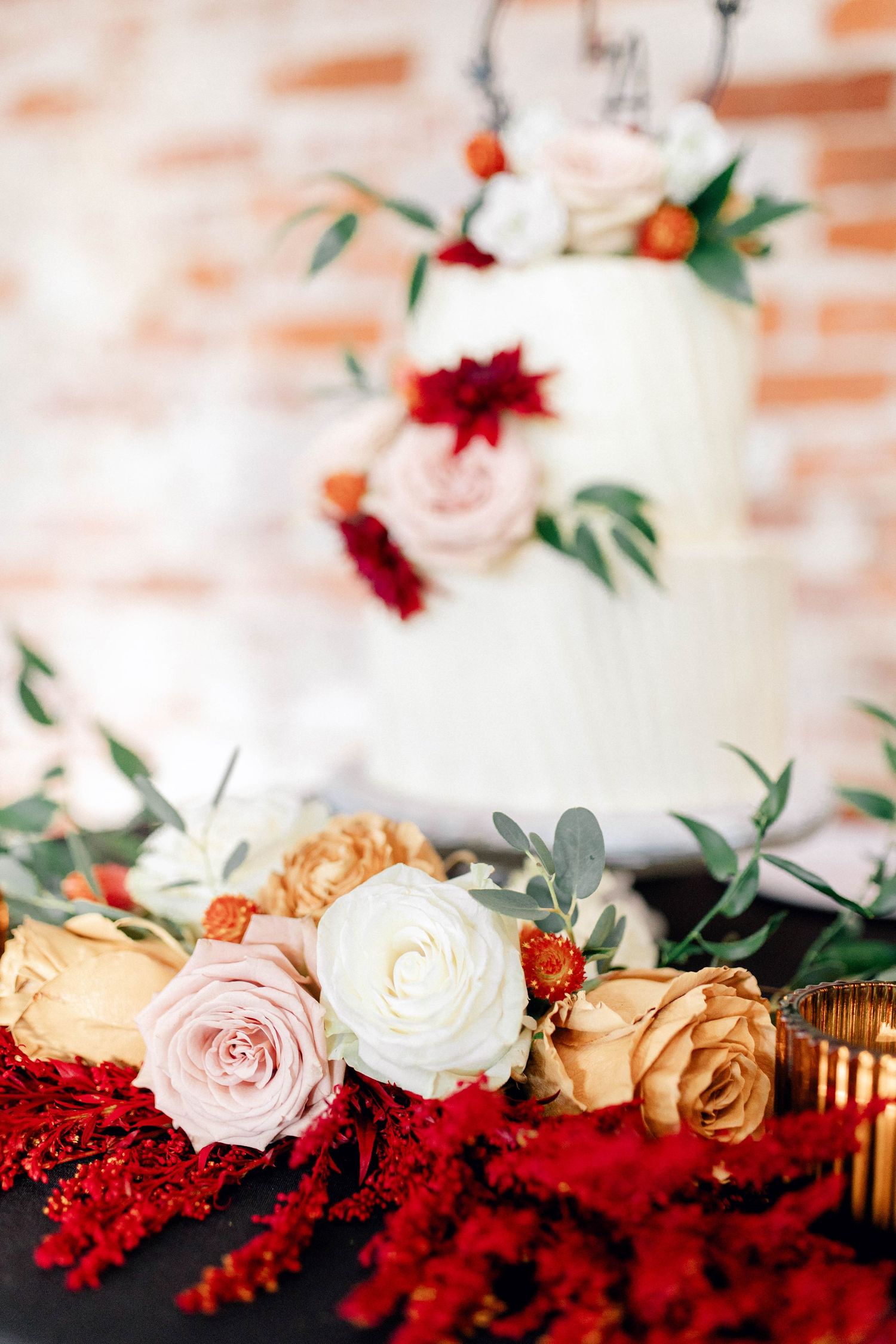 Wedding cake decorated with red and pink roses against a brick background.