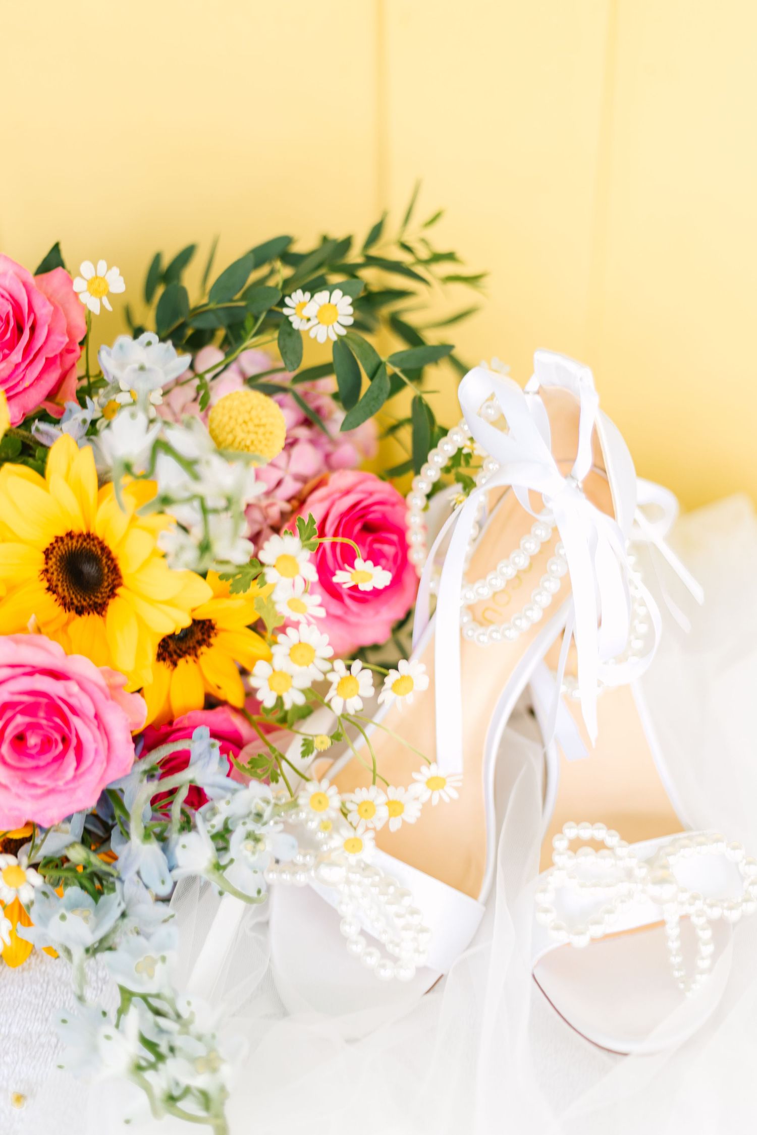 Colorful summer wedding bouquet with sunflowers and pink roses against a yellow background.