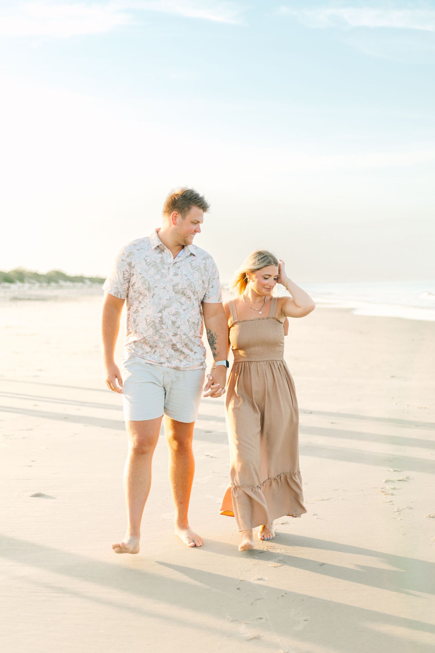 Couple walking hand in hand along the shoreline during golden hour.
