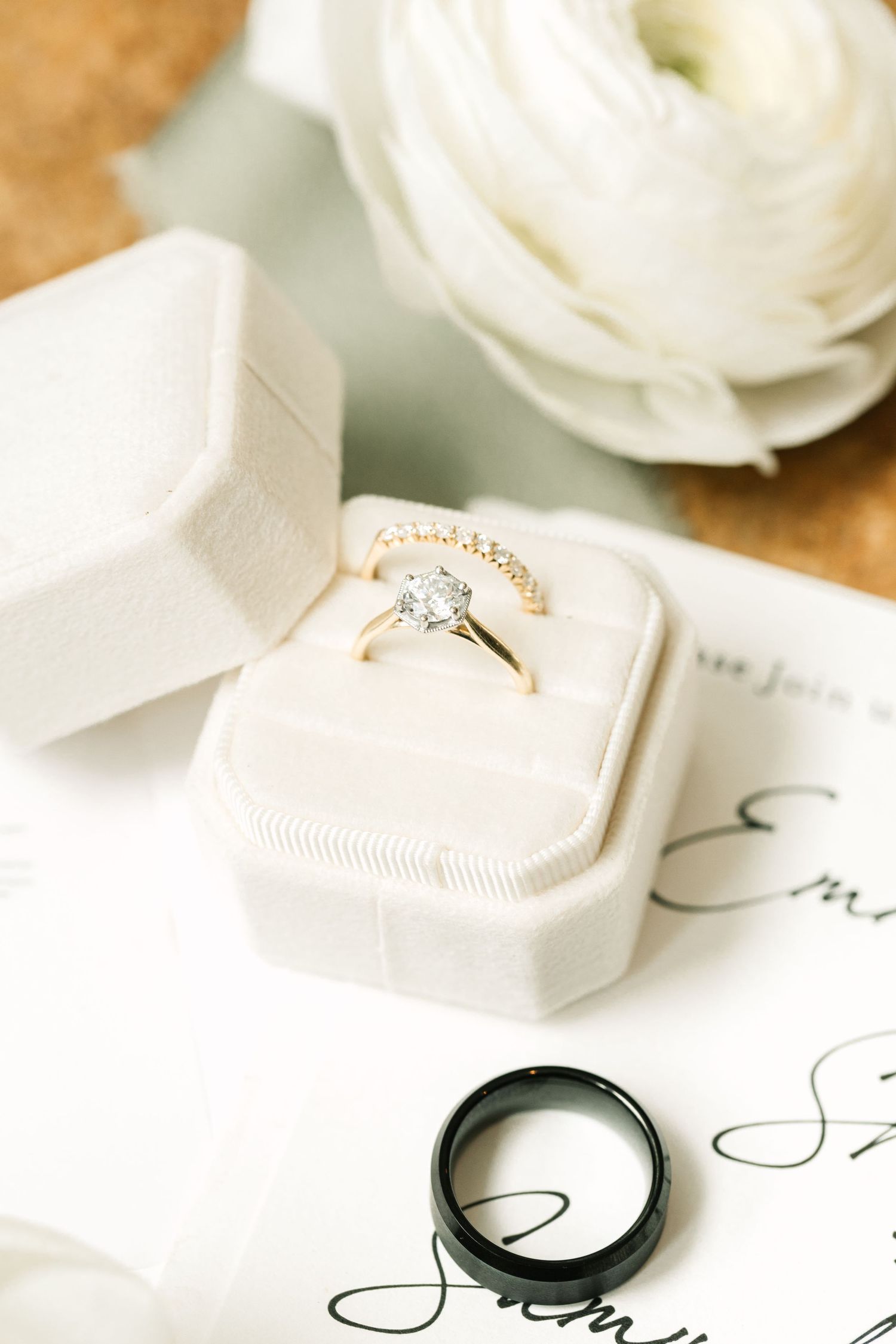 Wedding rings and engagement ring displayed with white flowers on elegant stationery.