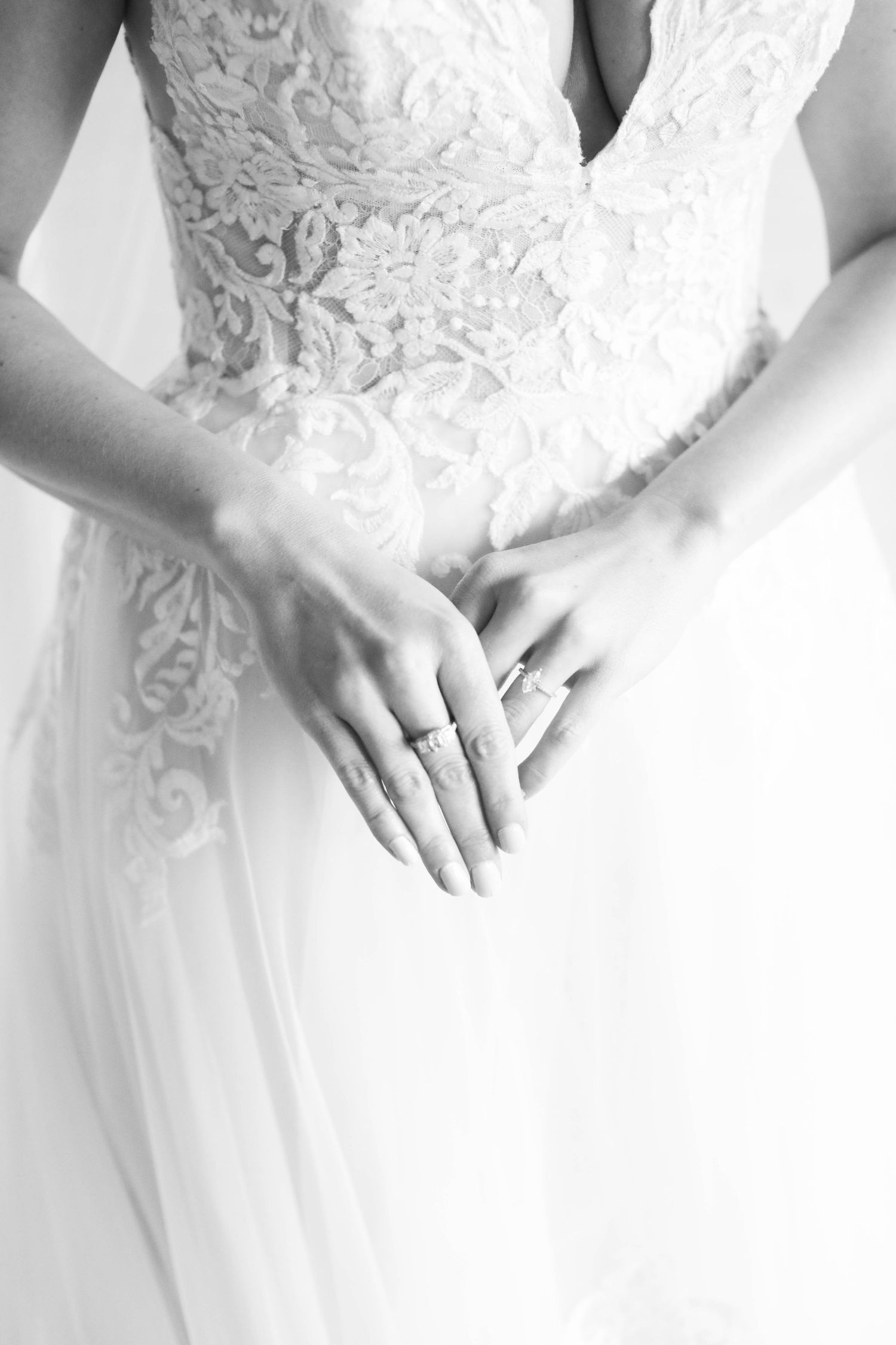Black and white close-up of hands wearing an engagement ring against a delicate lace wedding dress bodice.