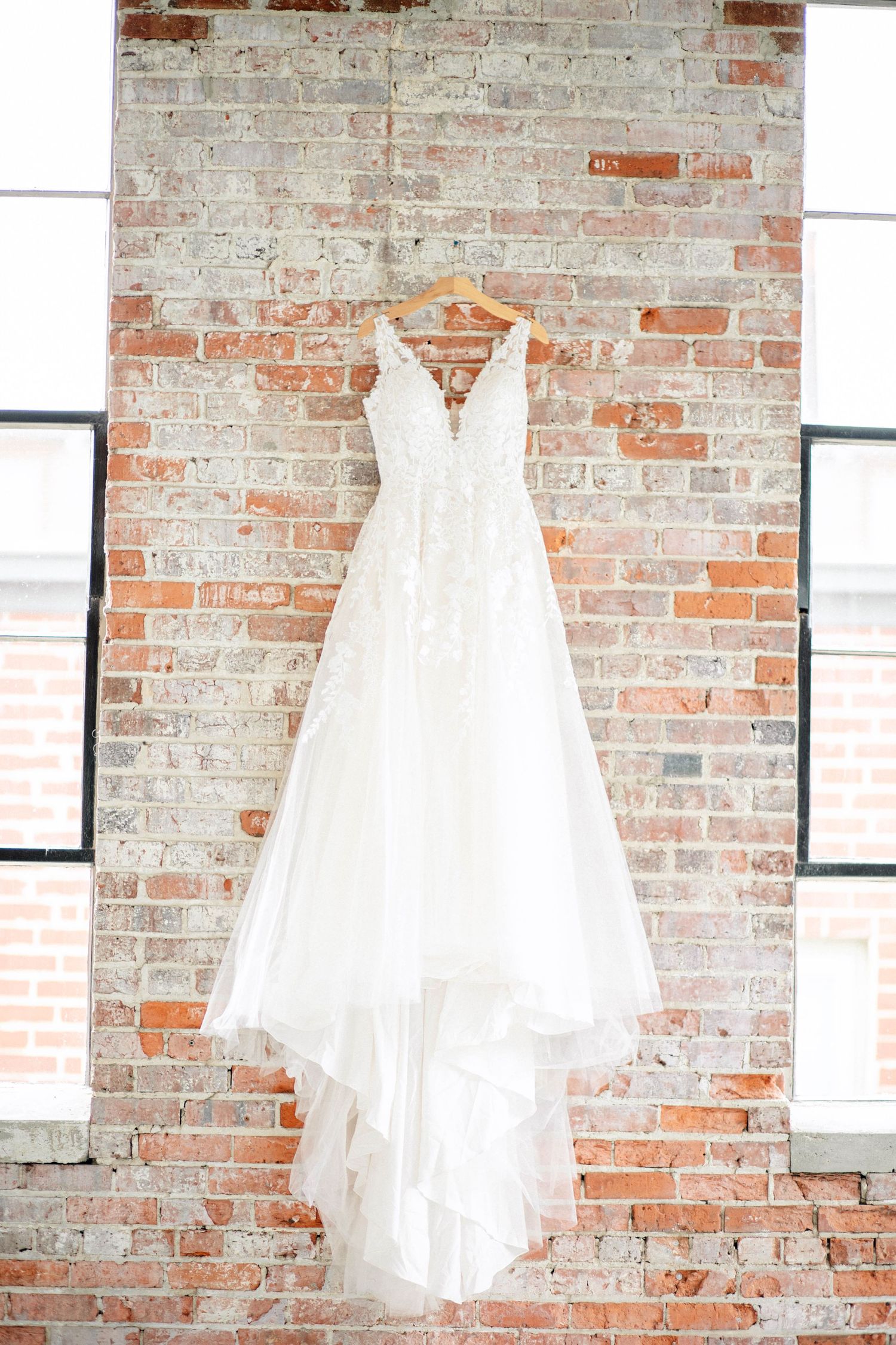 Wedding dresses displayed on hangers against an exposed brick wall.