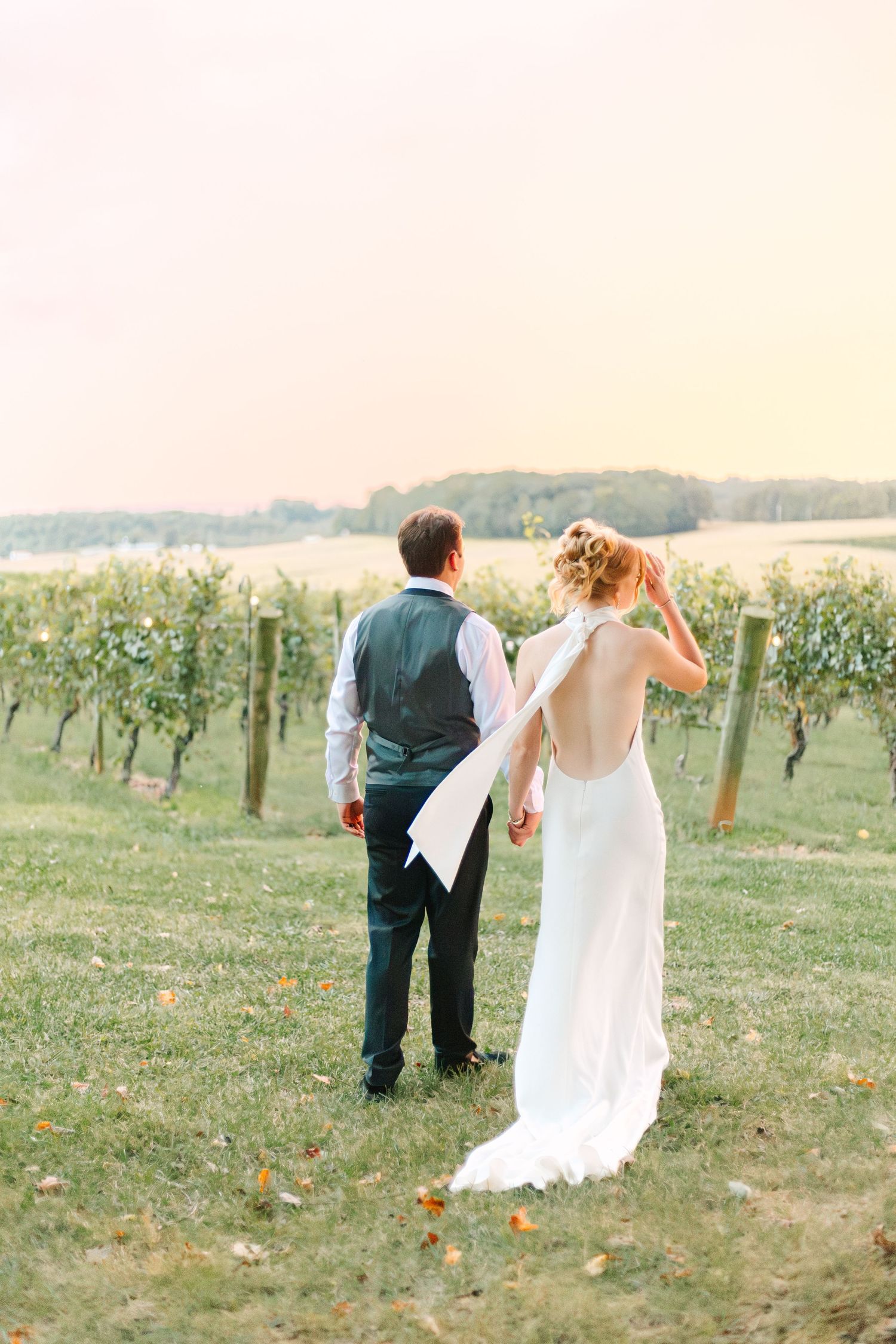 Couple walking through a scenic vineyard in wedding attire on their special day.