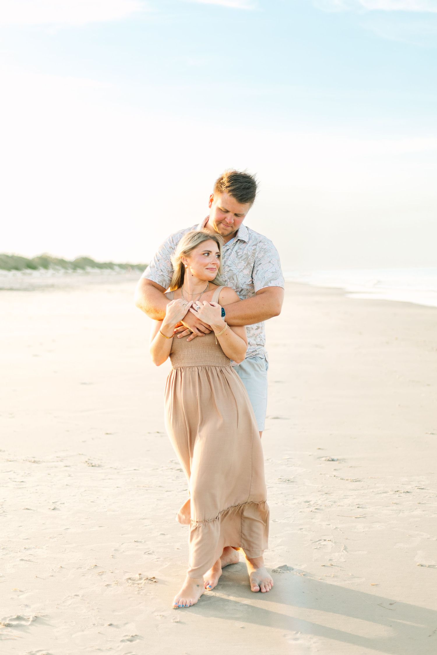Romantic couple poses together on a sandy beach at sunset.