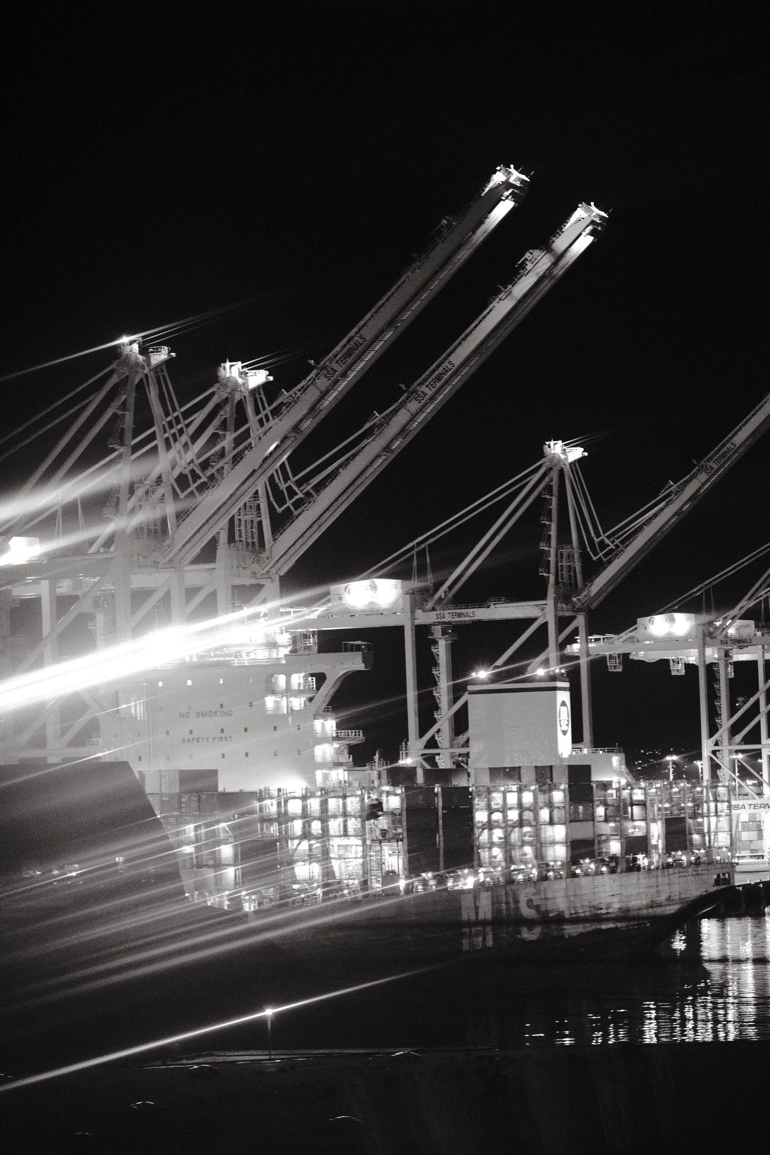 Industrial shipping port at night with illuminated cranes and cargo containers.