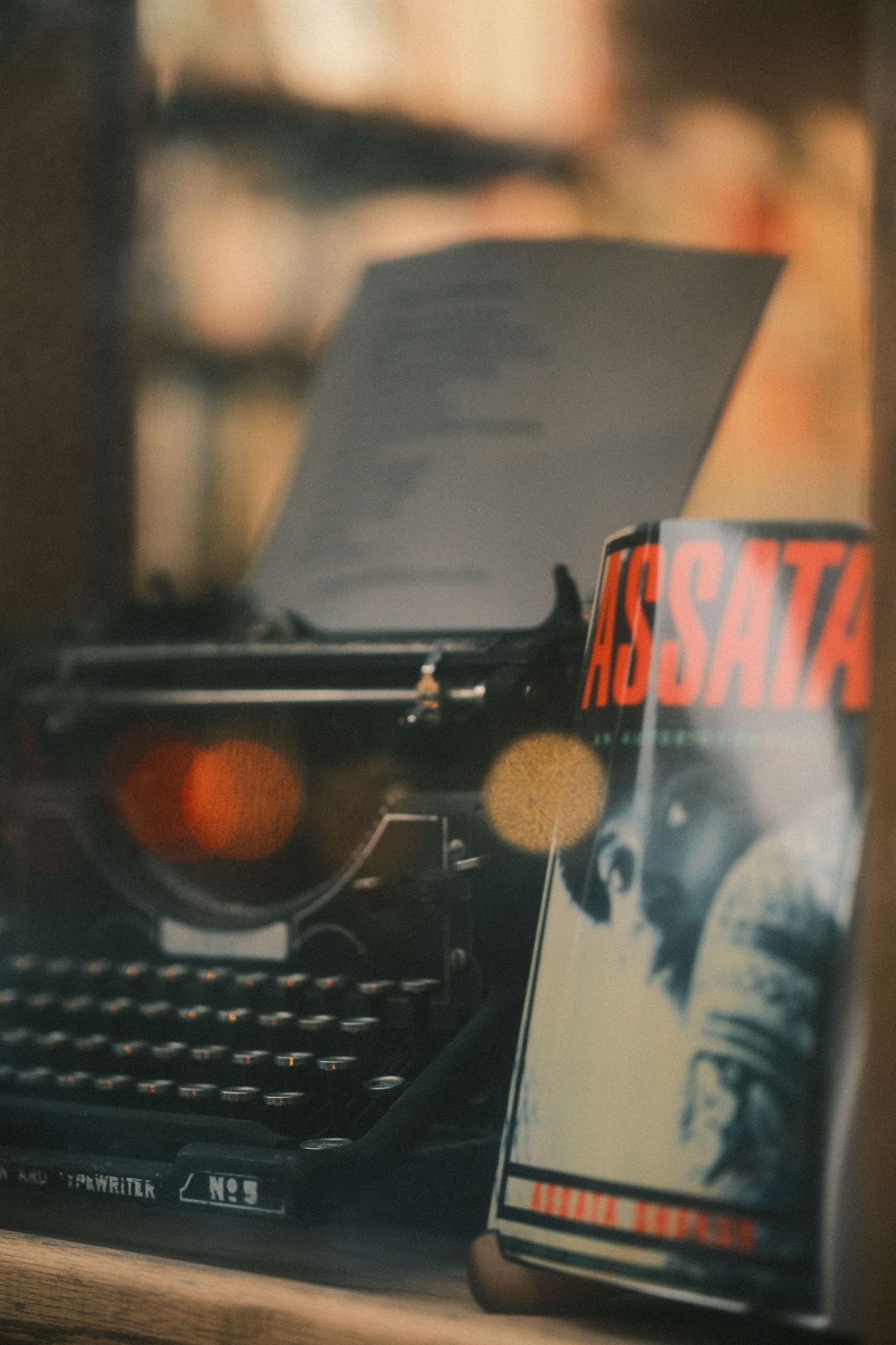 Vintage typewriter with books arranged on wooden surface in moody lighting.