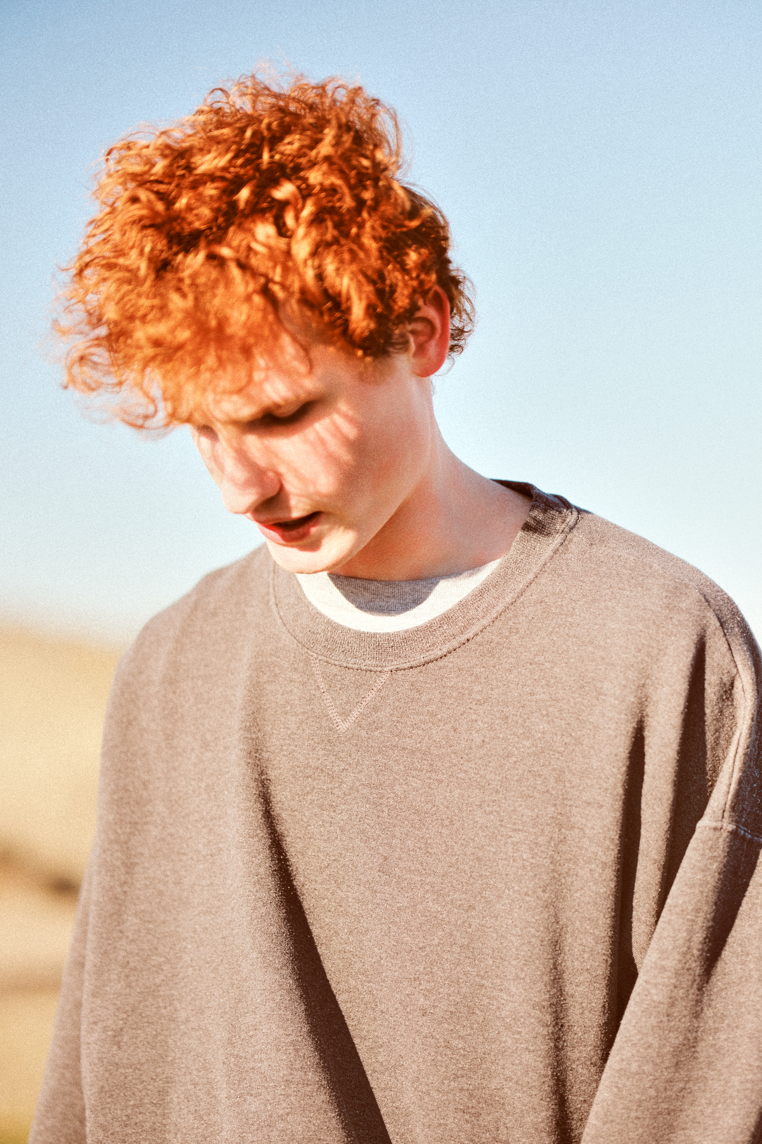 Minimalist portrait sequence showing bright orange curly hair against a pale blue sky.