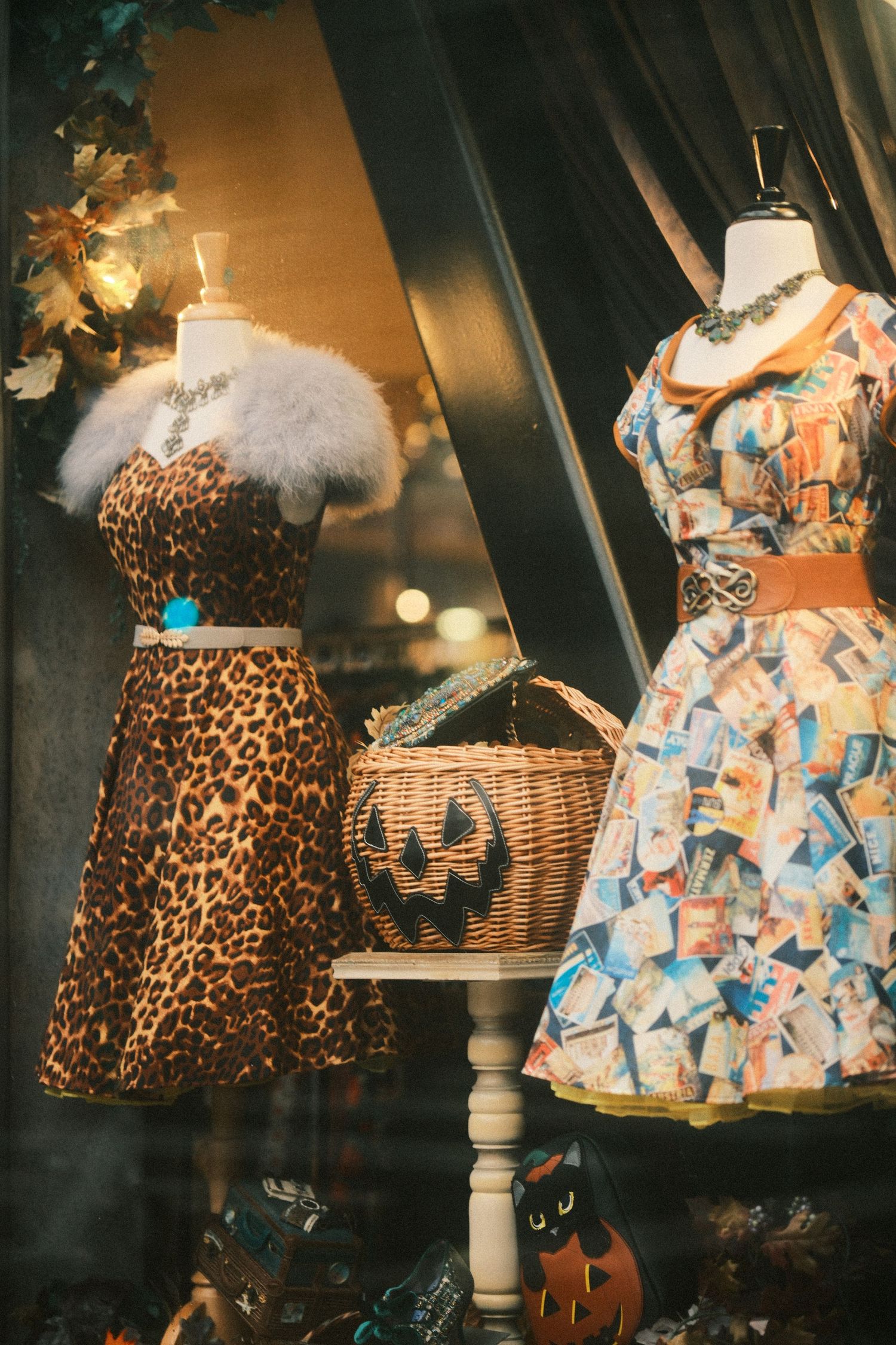 Retro window display featuring leopard print and patterned dresses with Halloween decorations.