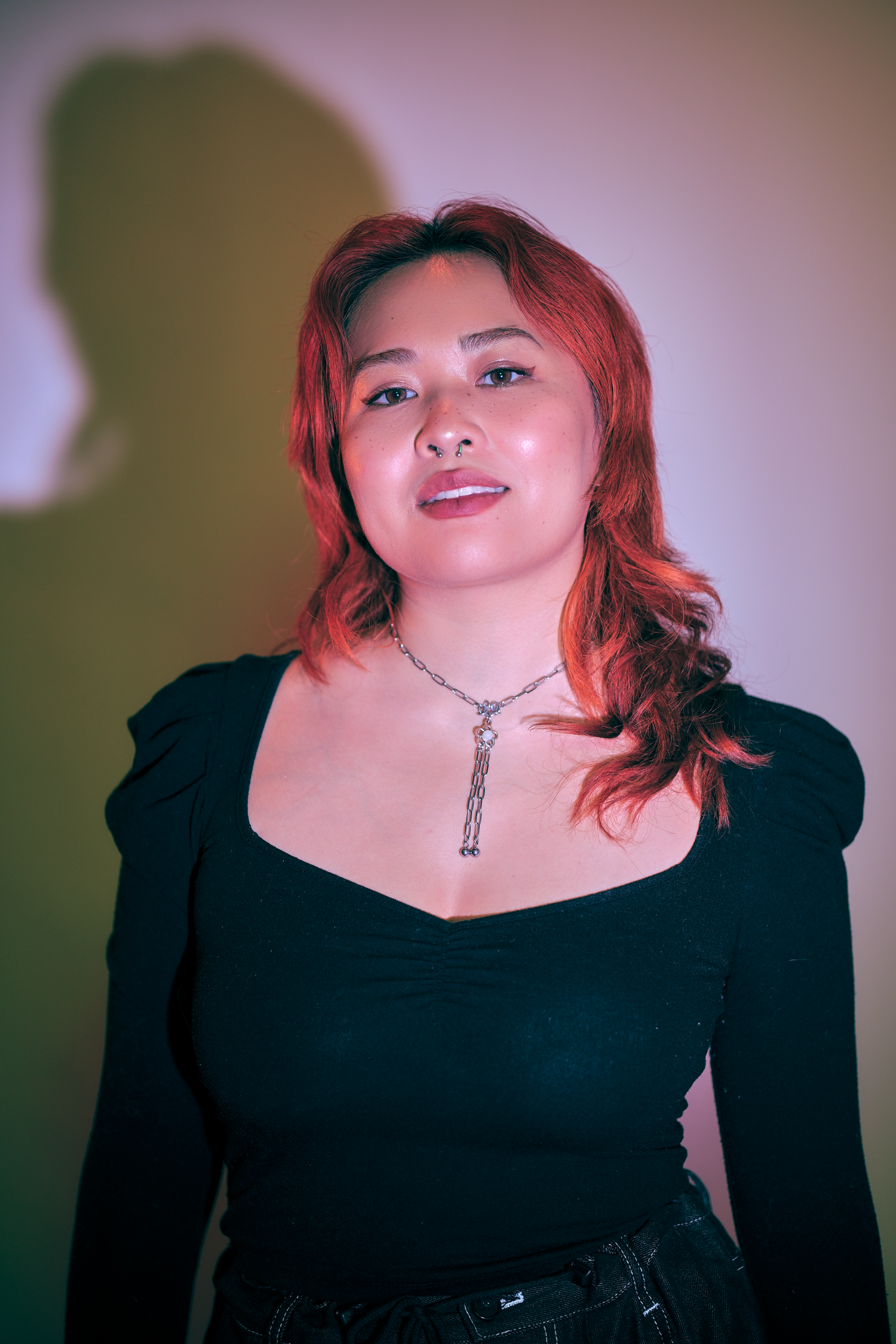 Portrait with red ambient lighting showing person in black top with key necklace.