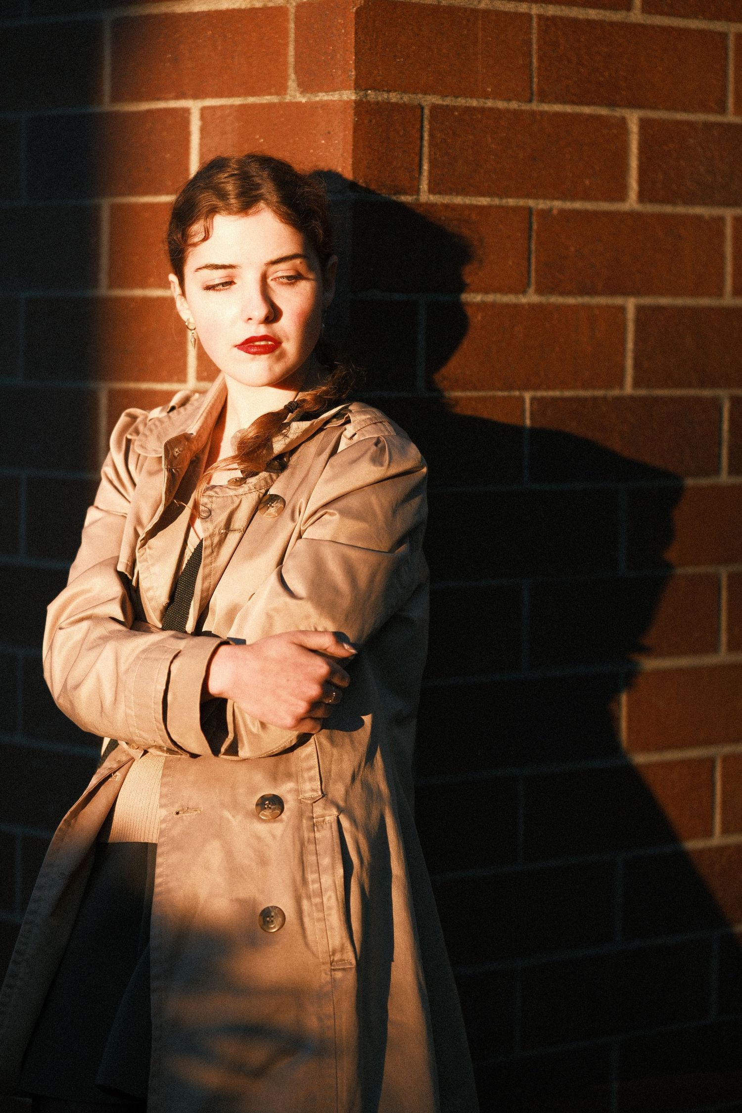 Dramatic sequence of someone posing against a brick wall in warm sunlight wearing a beige coat.