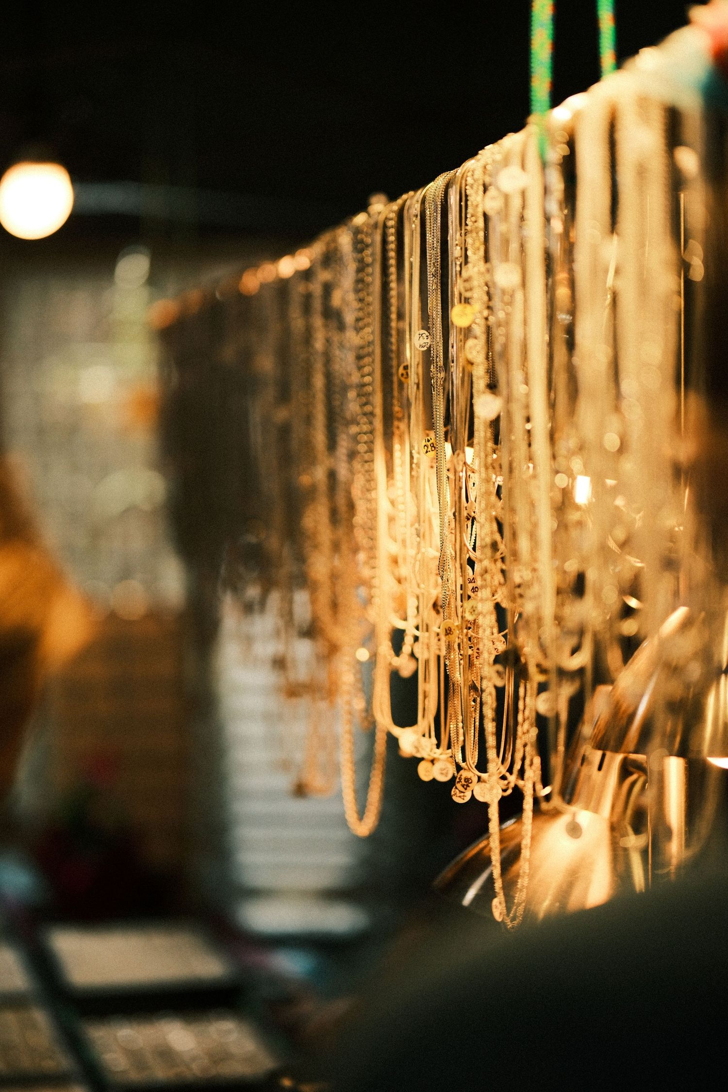 Hanging gold-toned jewelry or chains displayed in a row with soft bokeh lighting effects.