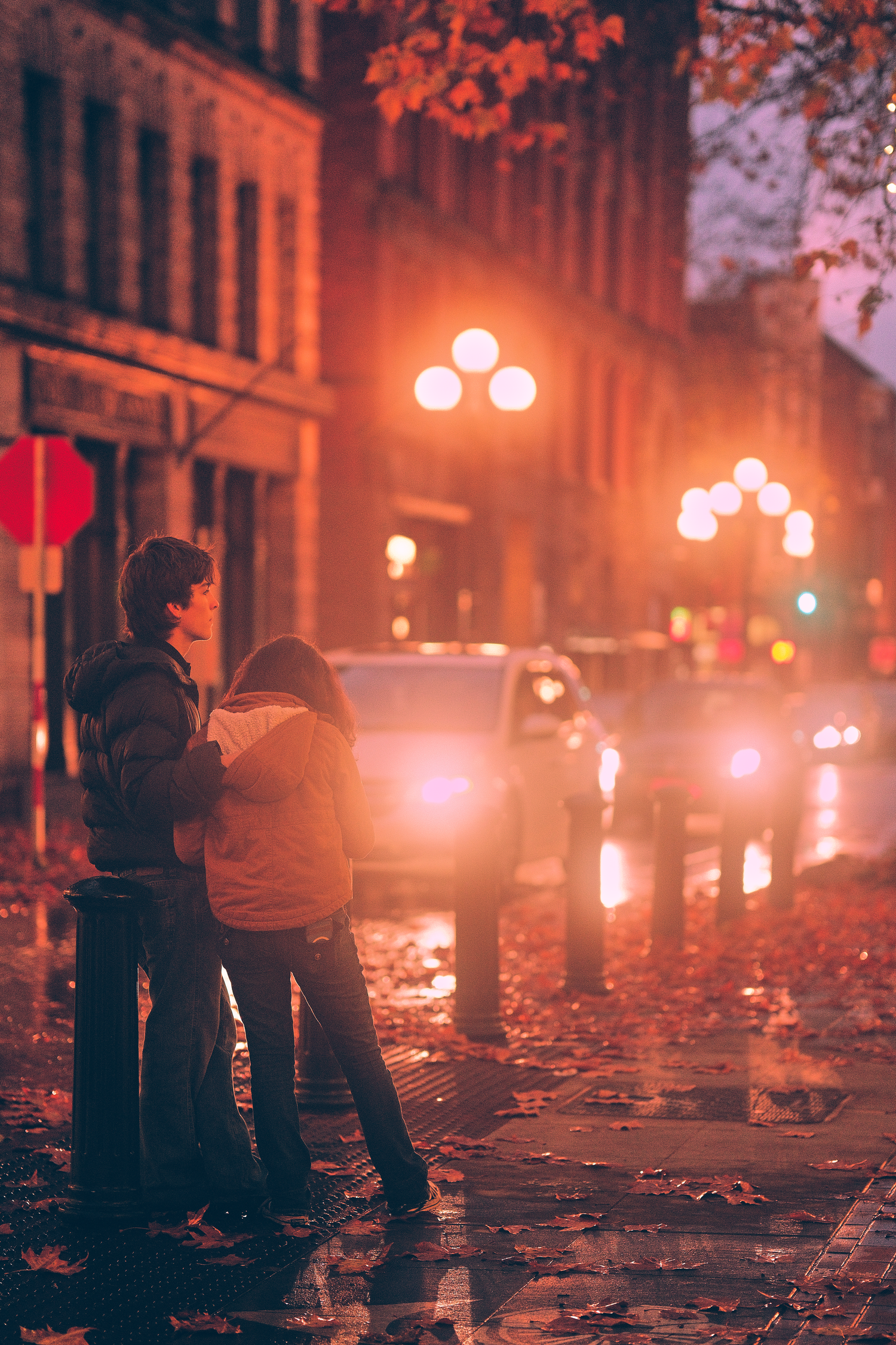 Silhouetted figures on a romantic evening street with glowing orange streetlights and fallen leaves.
