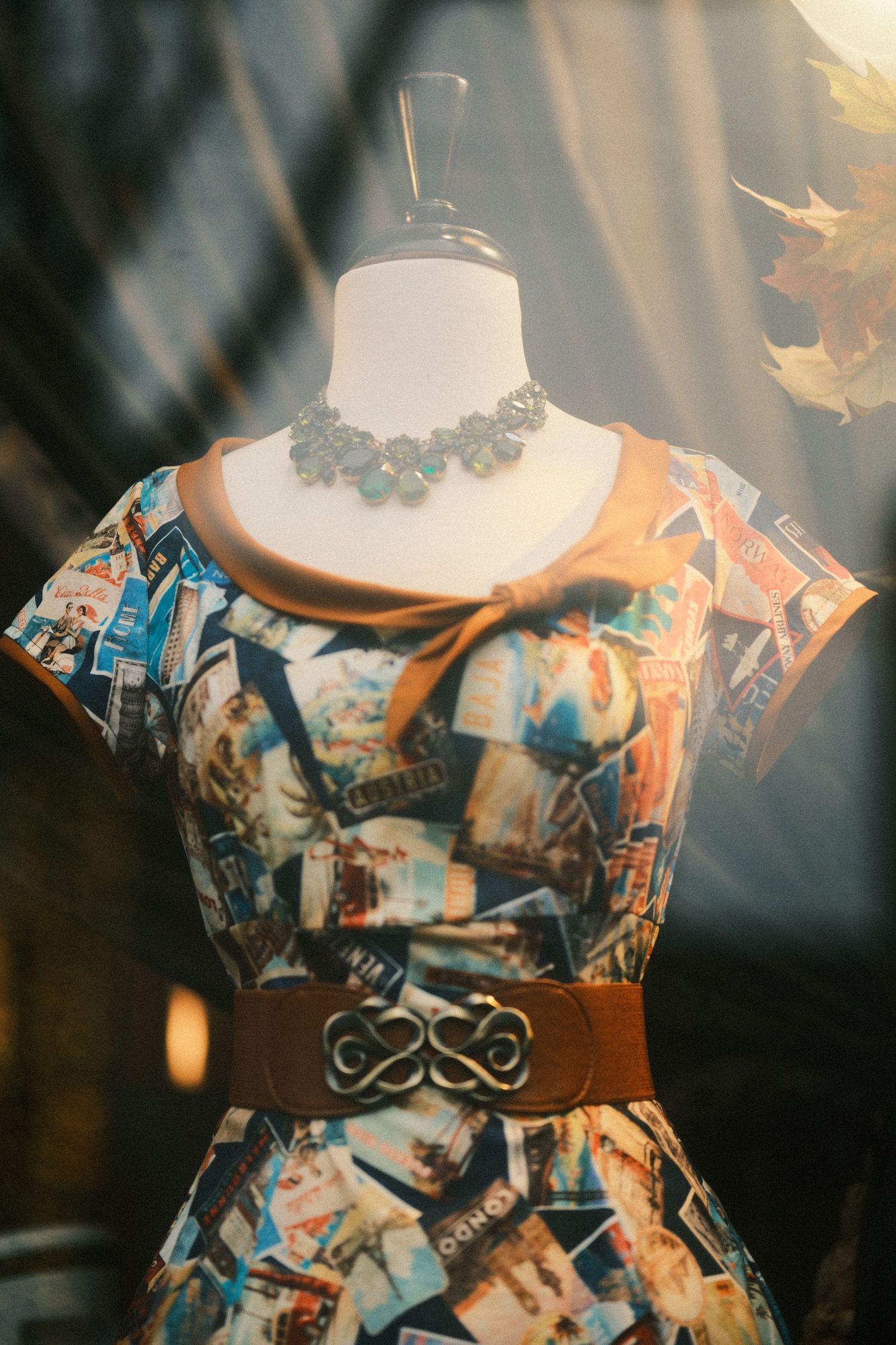 Vintage dress form displaying a patterned dress with statement necklace and belt.