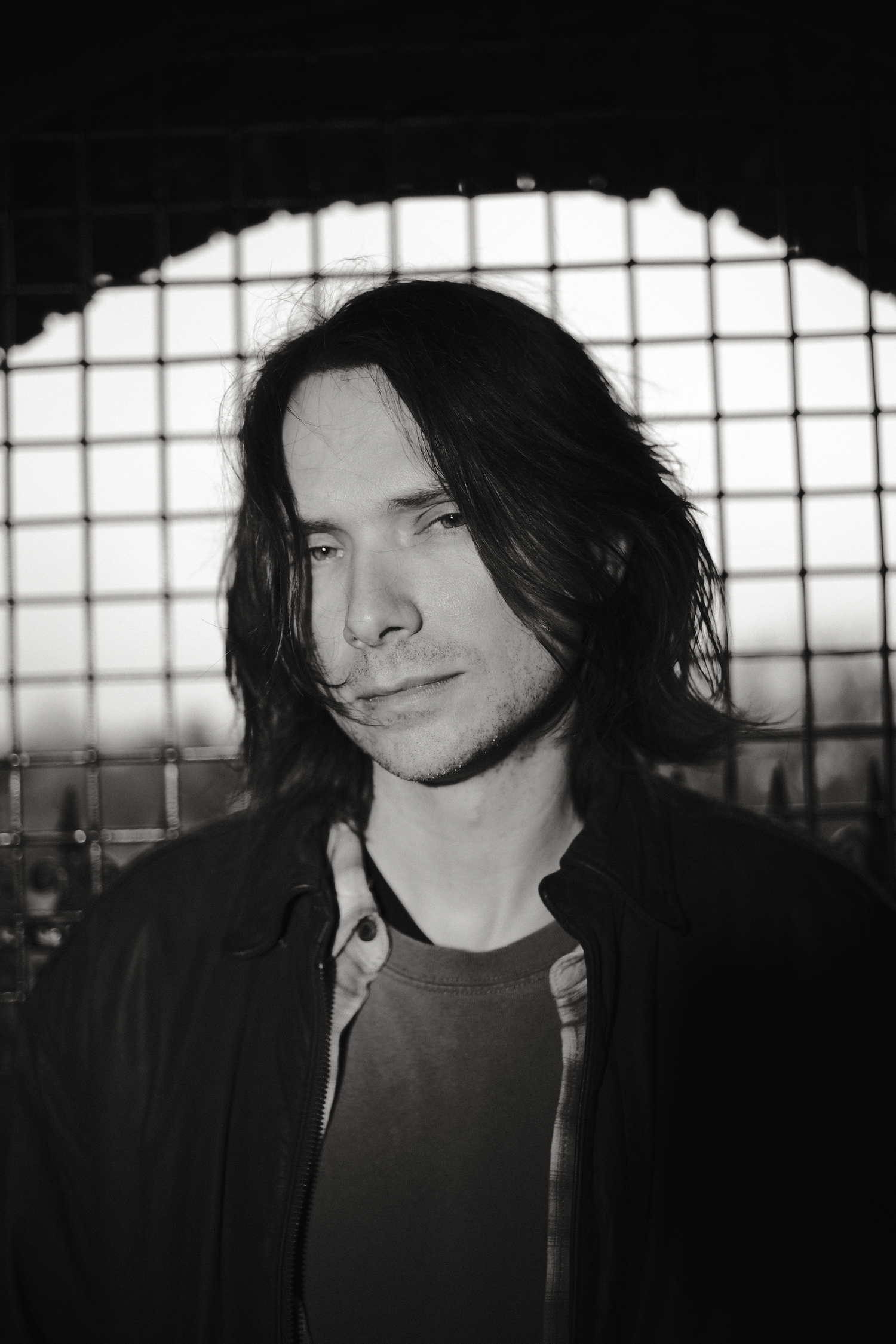 Black and white portrait series showing dark-haired figure in moody indoor lighting against industrial windows.