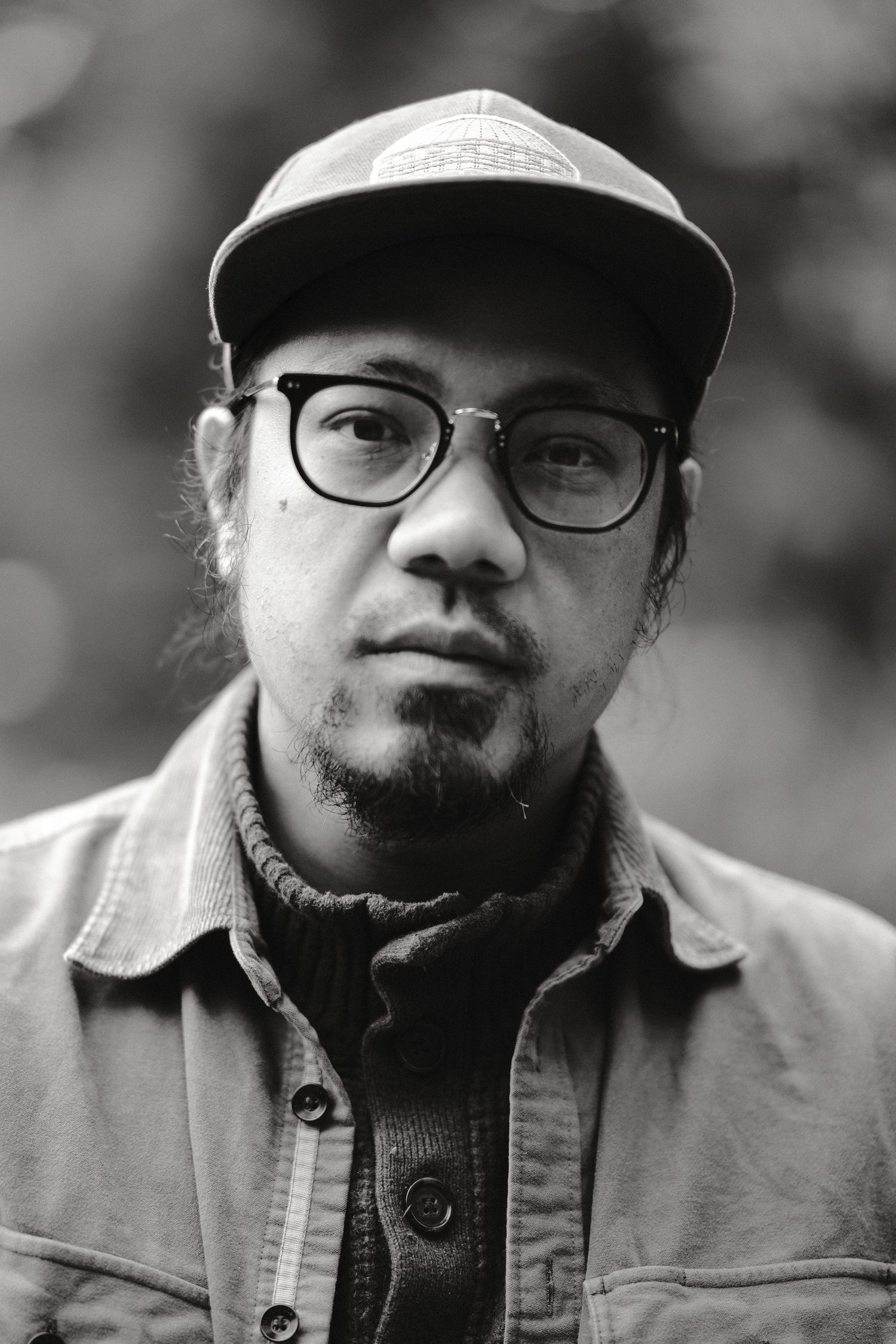 Black and white portrait of a person wearing glasses and a baseball cap in casual attire.