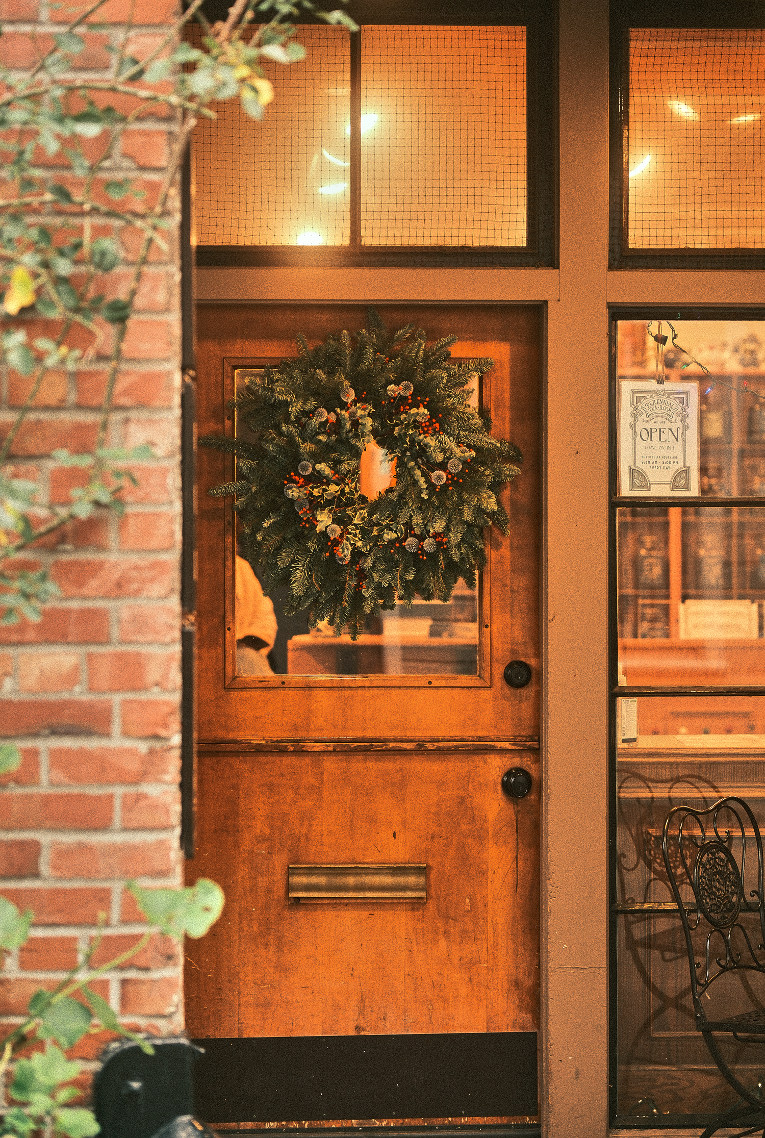 Warm wooden door with festive Christmas wreath and glowing lights in brick entryway.