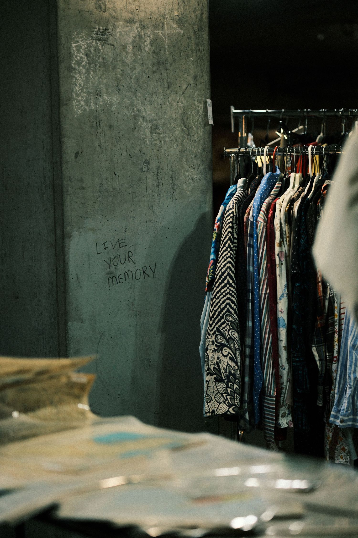 Clothing rack with patterned garments against a concrete wall with graffiti.