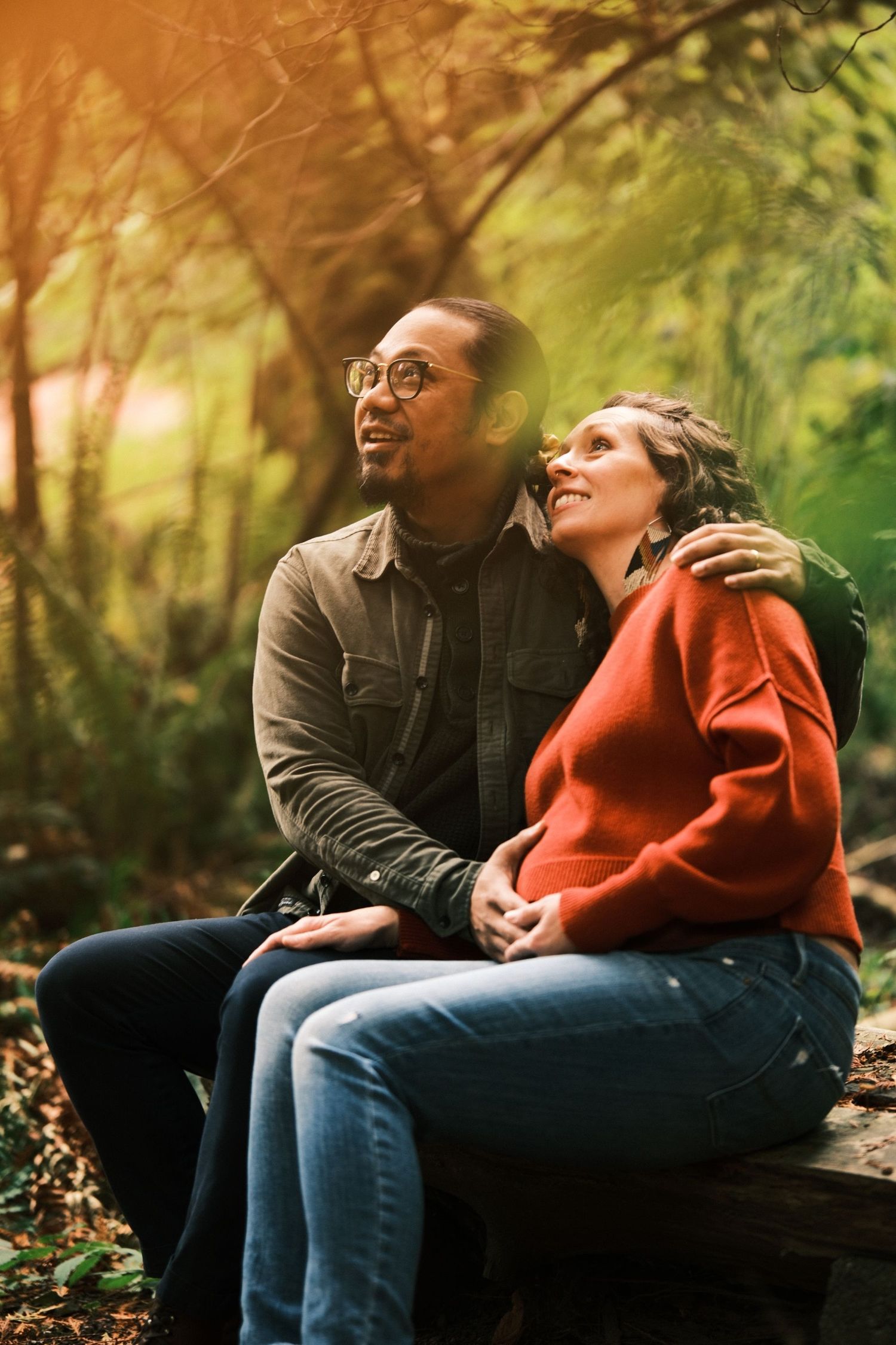 Couple sitting together outdoors in a natural setting with warm sunlit foliage.