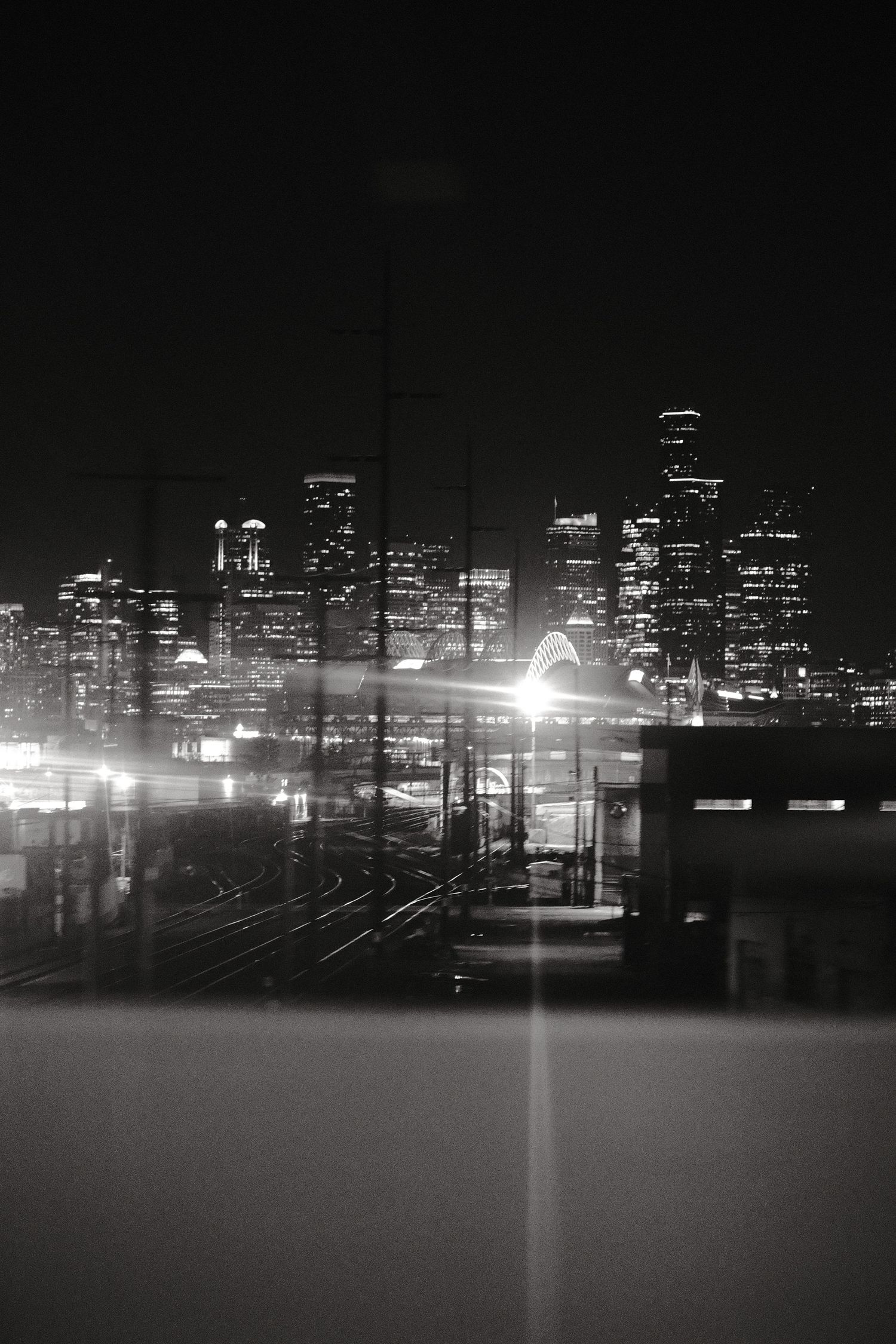 City skyline silhouetted against dark sky with bright lights reflecting across water at night.