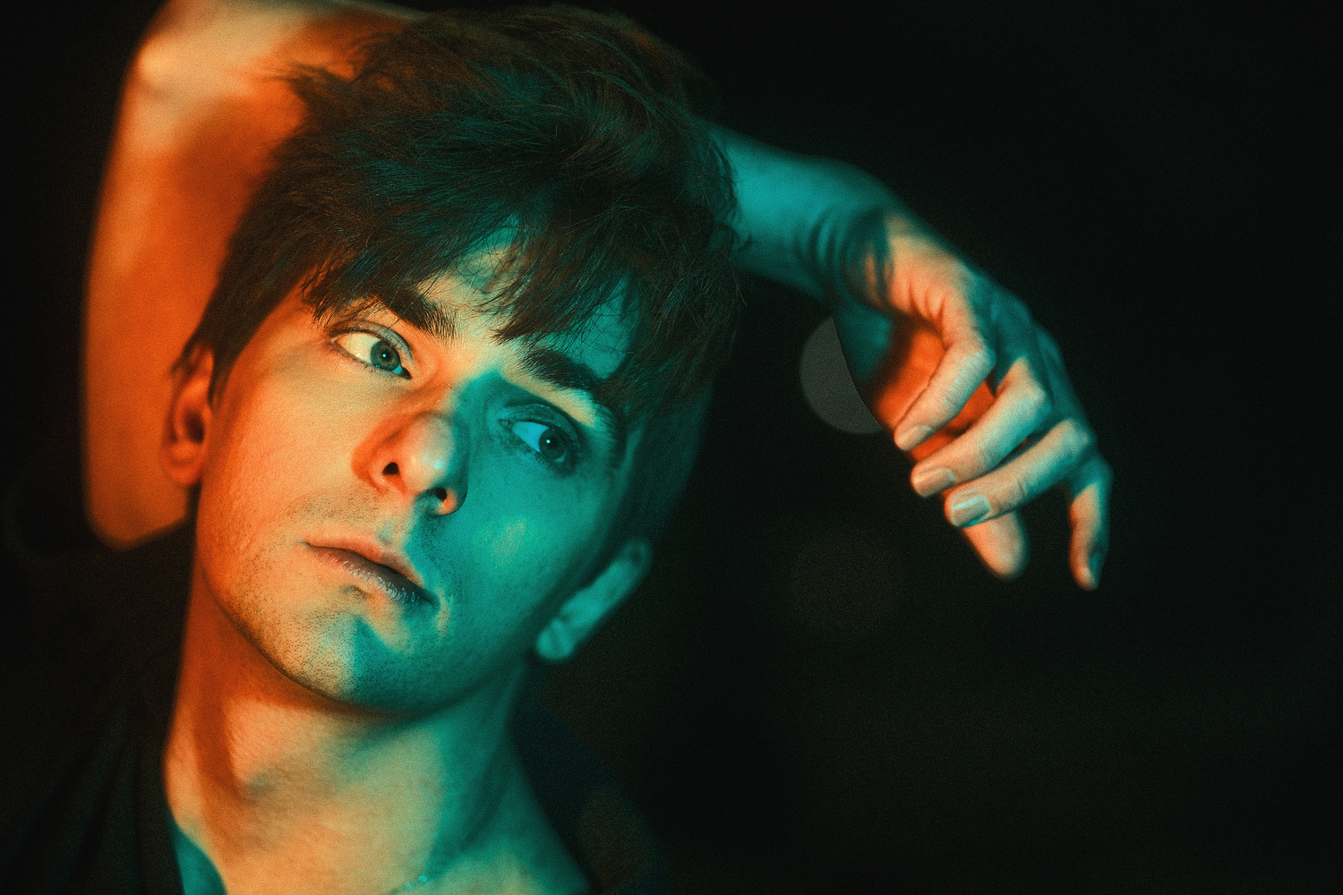 Artistic portrait with dramatic blue and orange lighting in a dark setting.