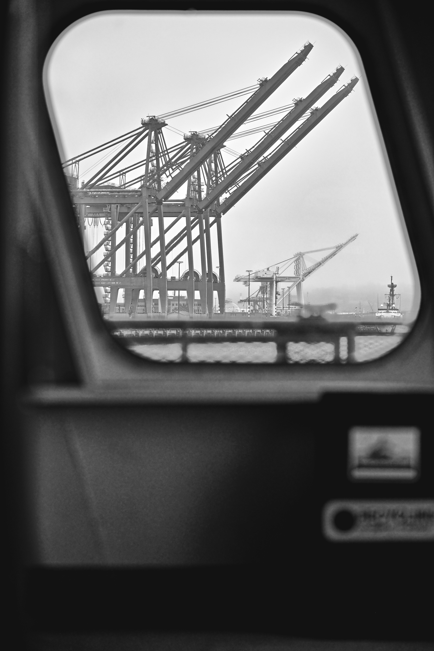 Industrial shipping cranes viewed through window frame in black and white.