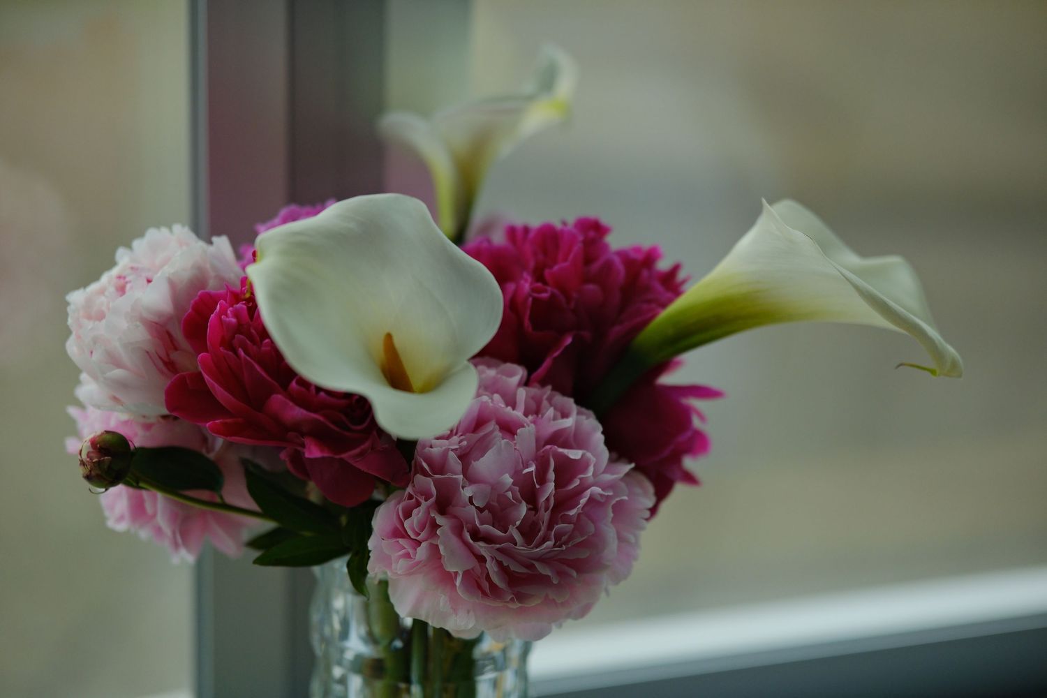 Elegant floral arrangement with pink carnations and white calla lilies in vase.