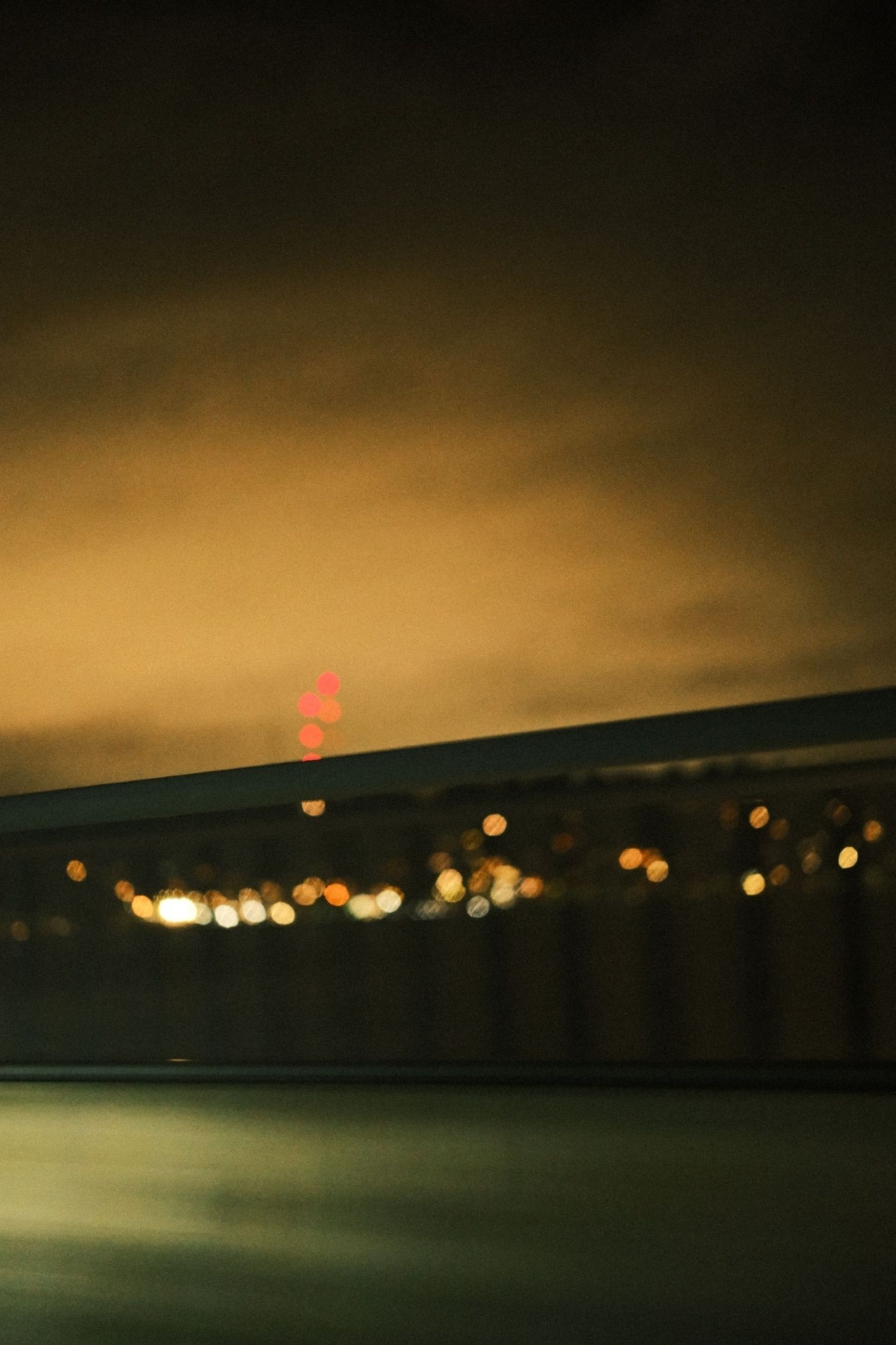 Distant city lights create bokeh effect across dark water at night with warm tones.