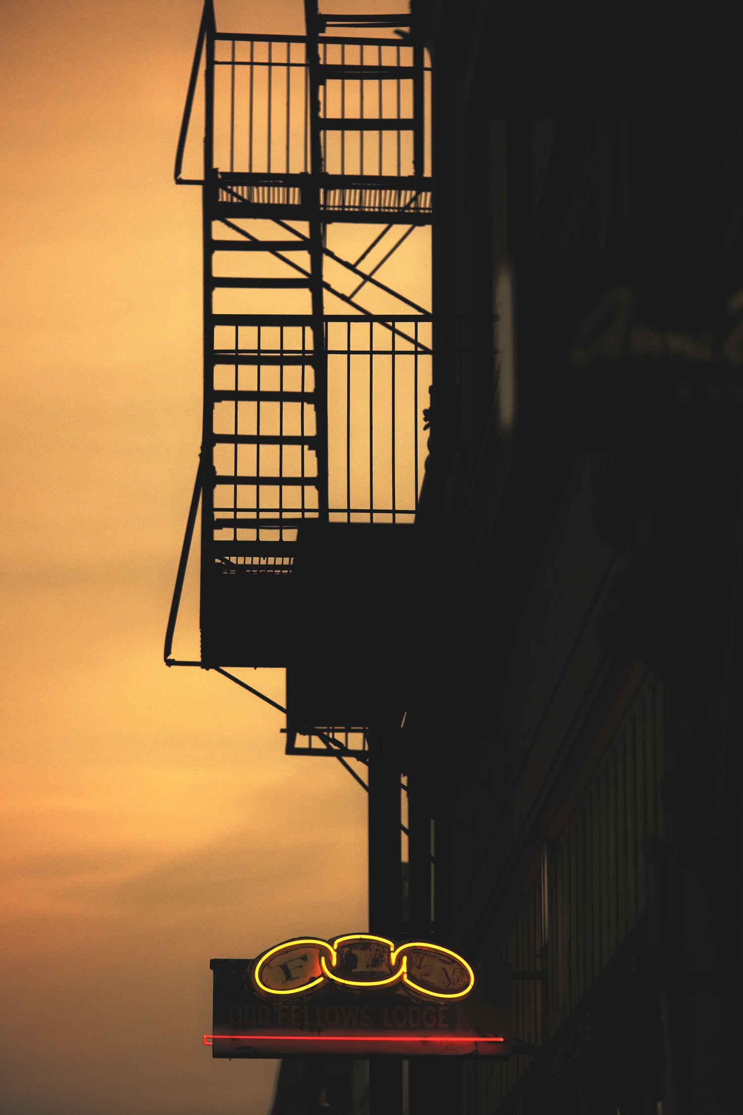 Silhouette of fire escape stairs against orange sunset sky.