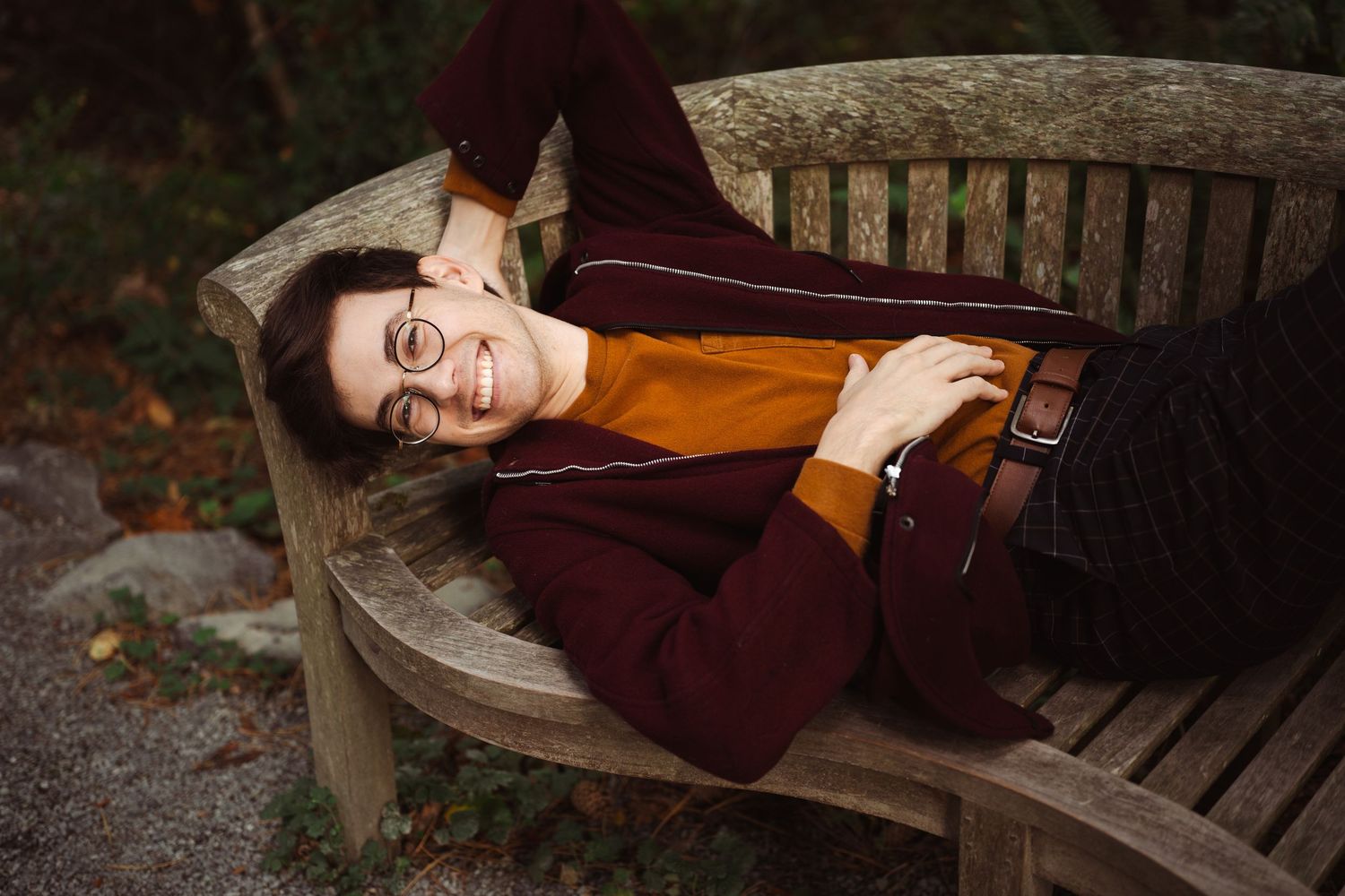 Person relaxing on a wooden bench surrounded by autumn leaves.