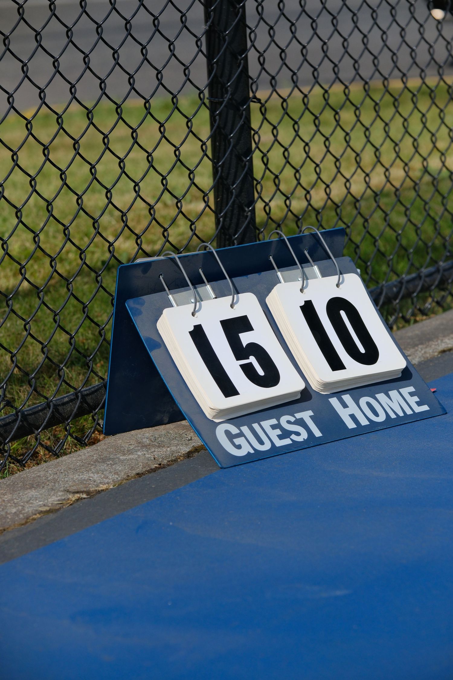 Sports scoreboard showing Guest 5 Home 10 mounted on chain link fence.
