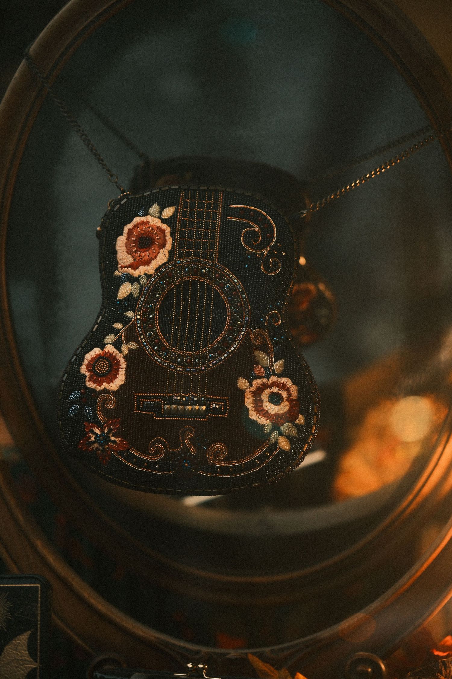 Decorative black guitar pendant with floral embellishments viewed through a circular frame.