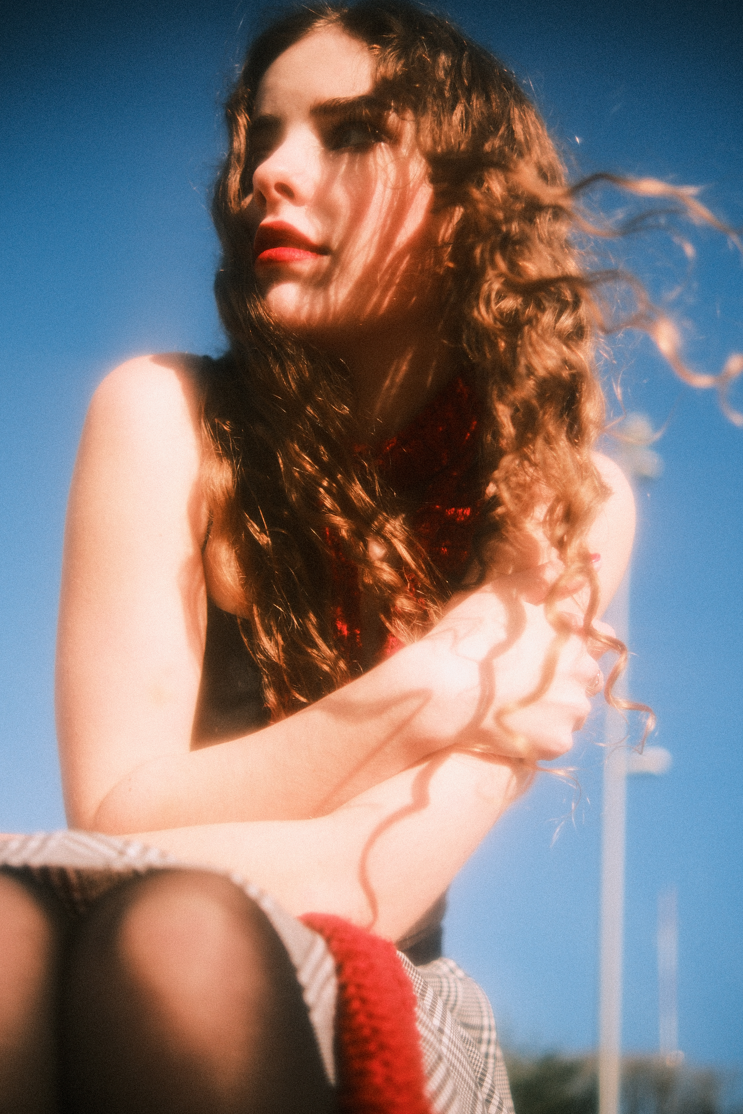 Artistic portrait series in warm tones showing curly hair and red lipstick against a blue sky background.