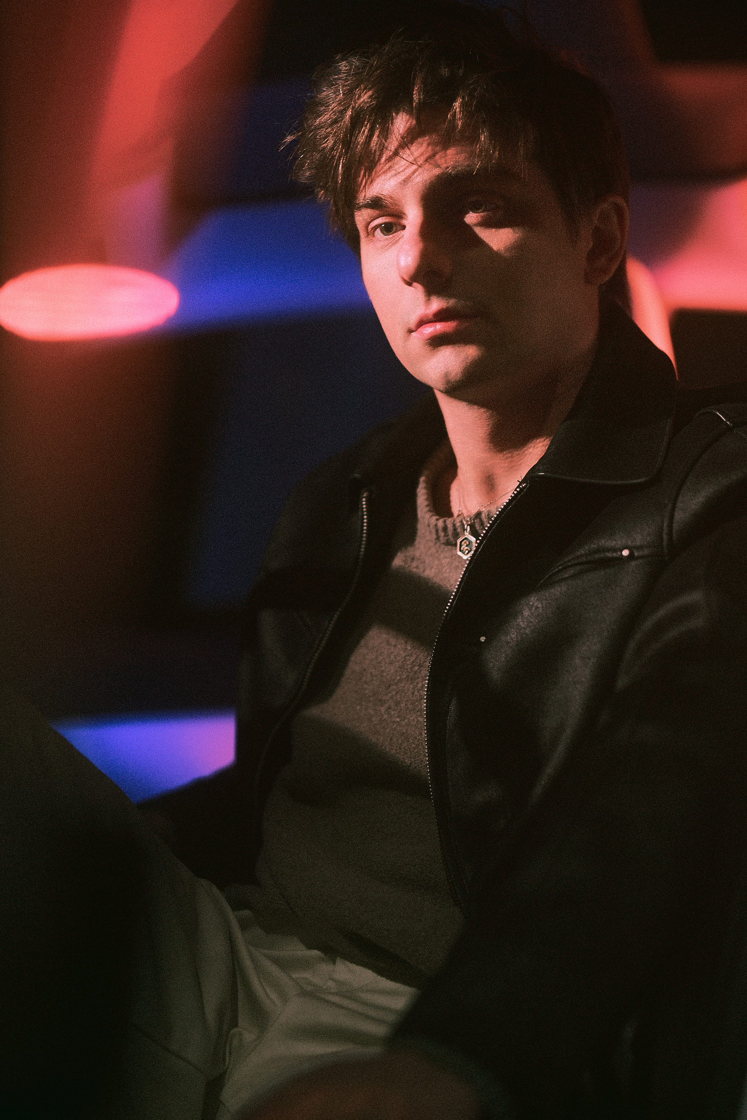 Moody portrait in dark lighting with blue and red ambient glow.