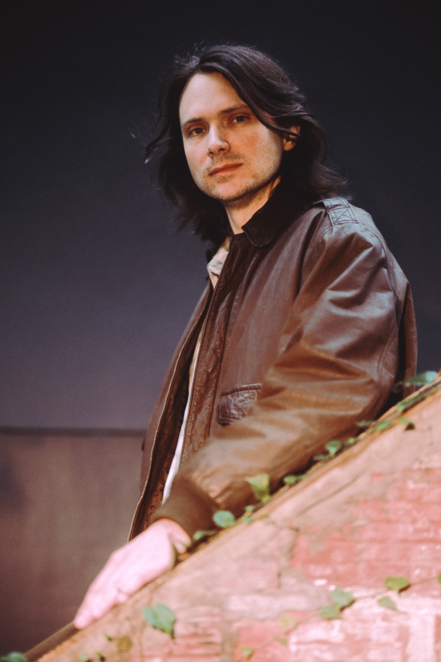 Portrait shot against dark background with leather jacket and long hair.