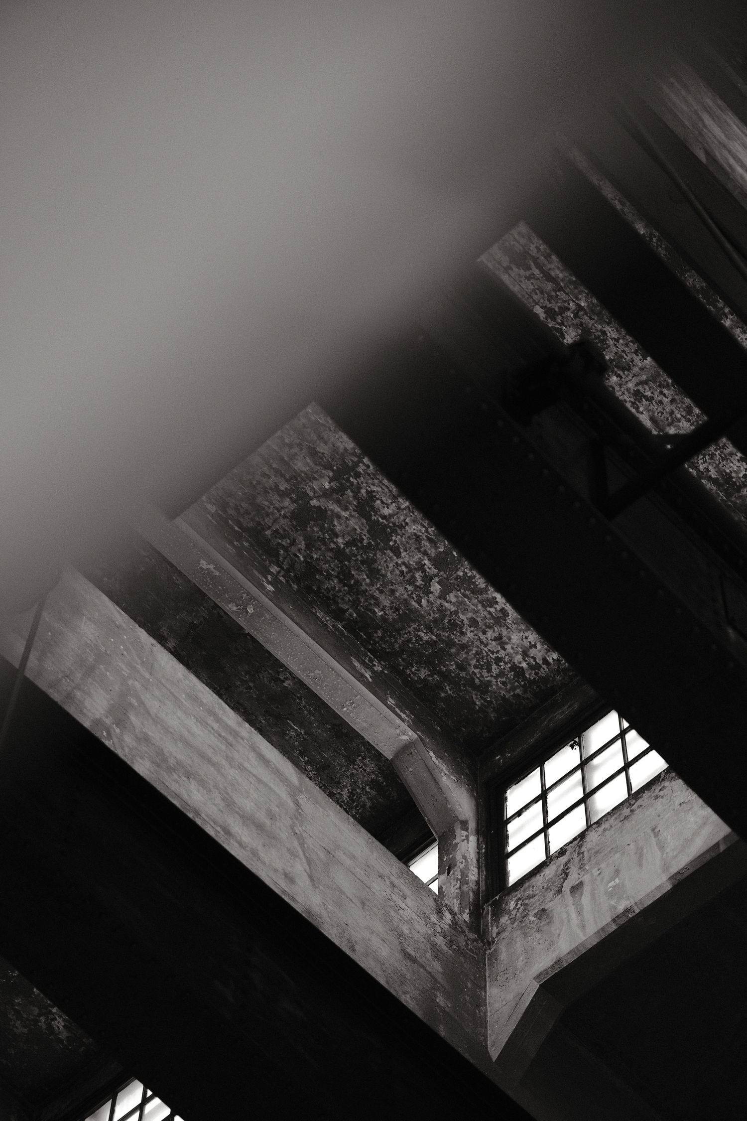 Dramatic black and white image of a window frame casting angular shadows in an abandoned building.