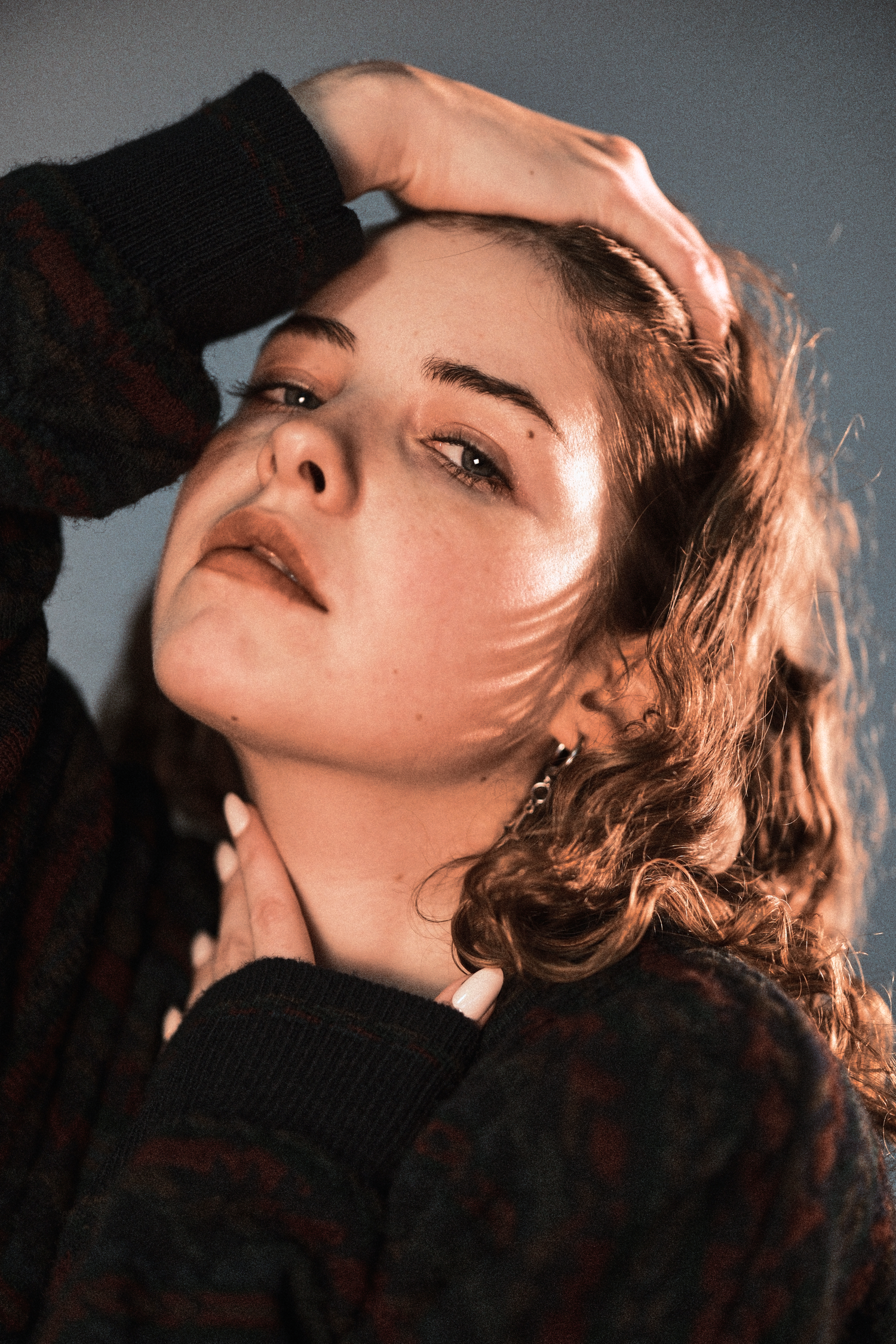 Artistic portrait of a person in dramatic lighting with eyes closed and hand near face.