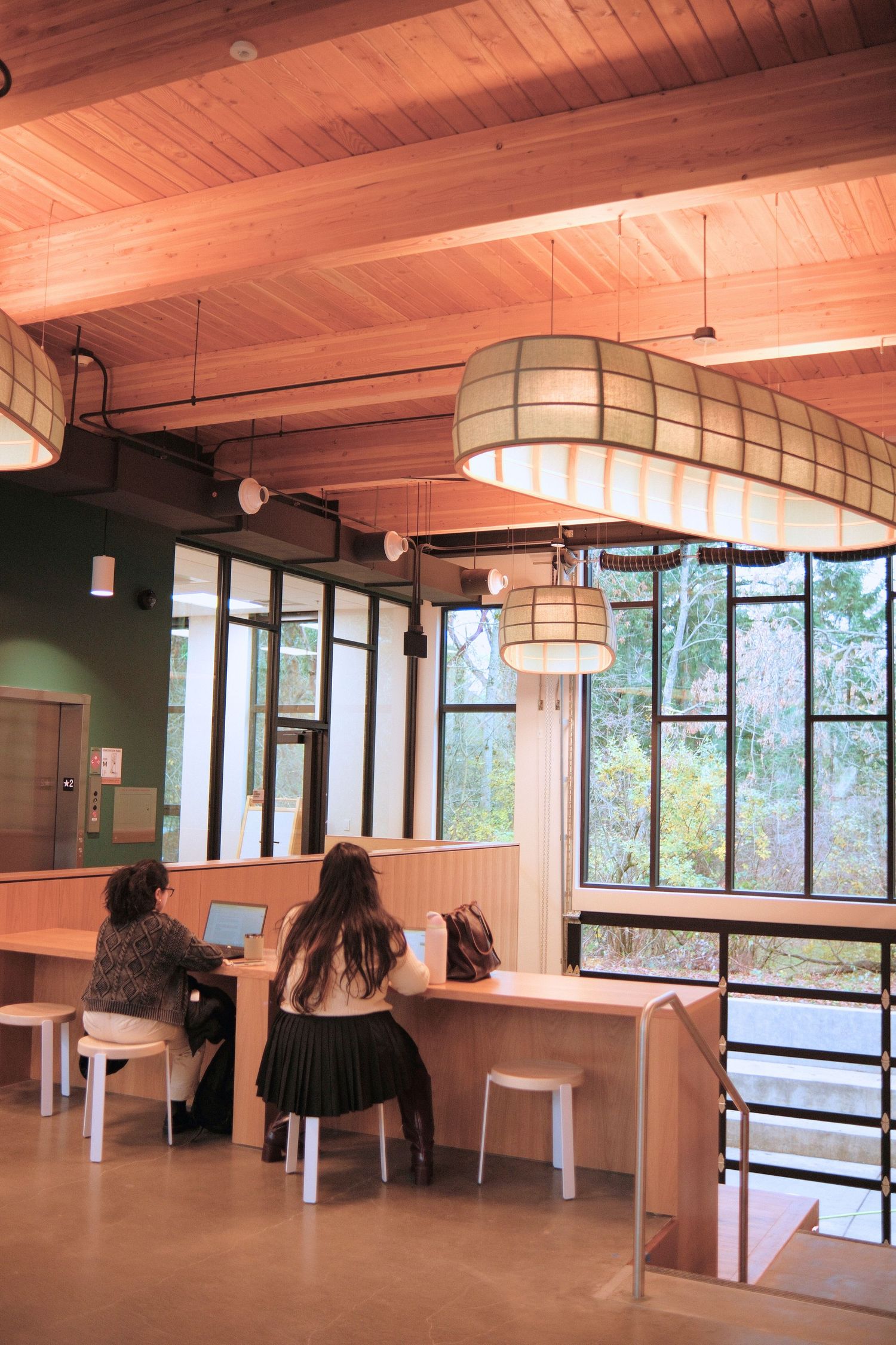 Modern office space with wooden ceiling beams, large windows, and pendant lighting.