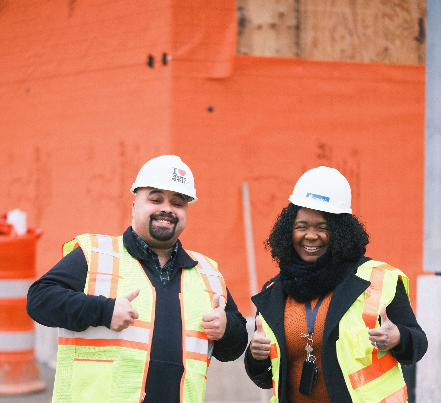 Construction workers in safety vests and hard hats giving thumbs up gestures at a worksite.