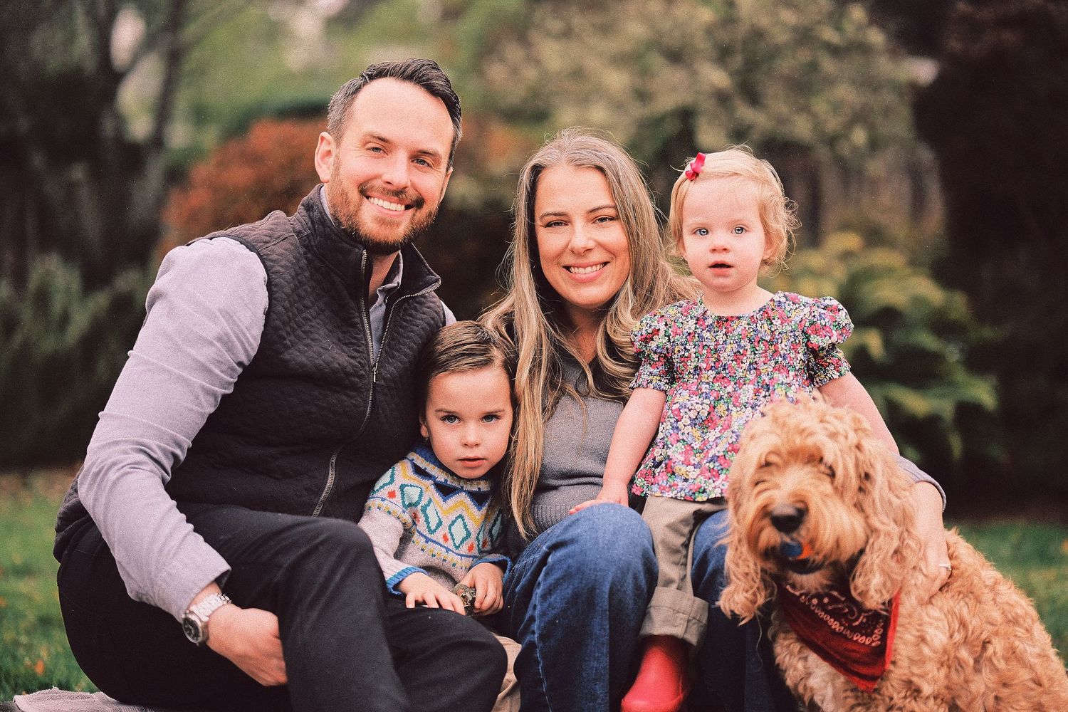 Happy family and their golden retriever dog posing together outdoors in a park setting.