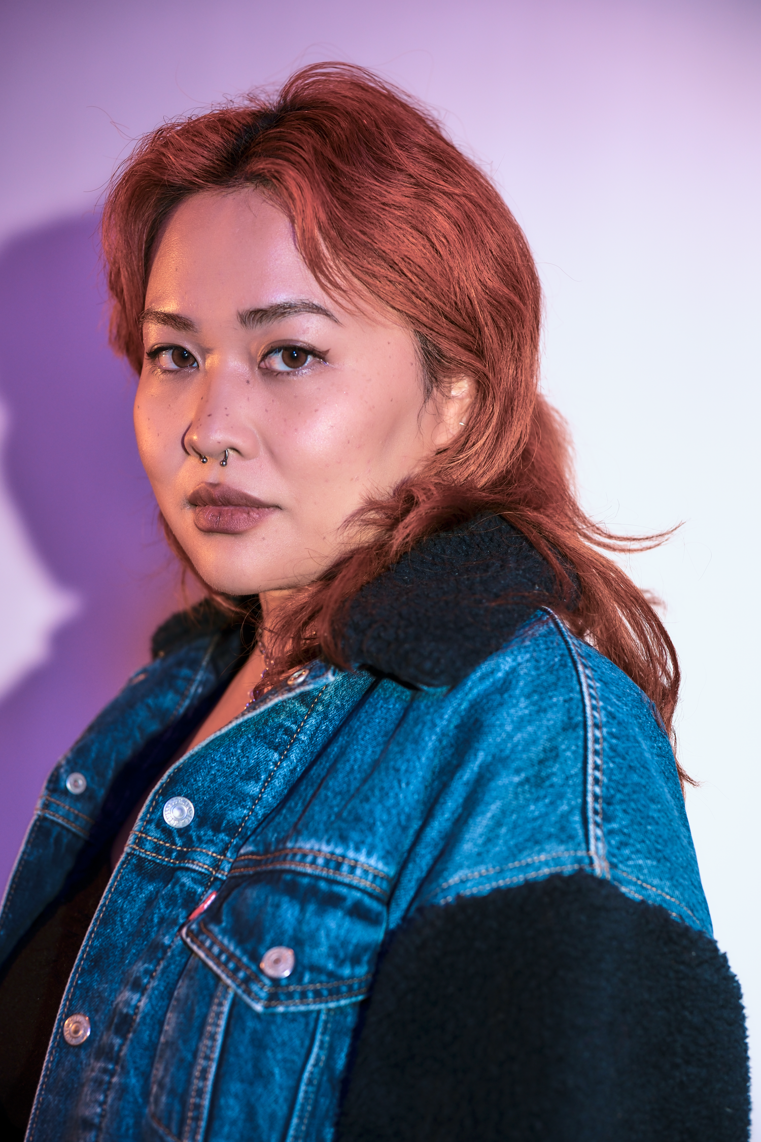 Portrait against purple backdrop wearing denim jacket with dramatic lighting.