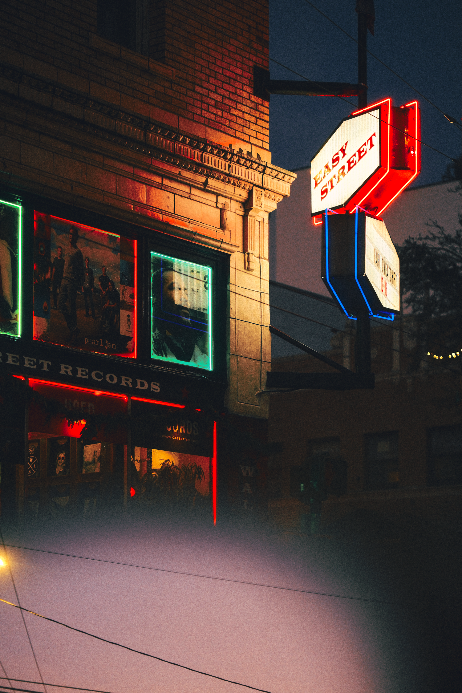 Neon signs and storefronts illuminated at dusk on a brick building facade.