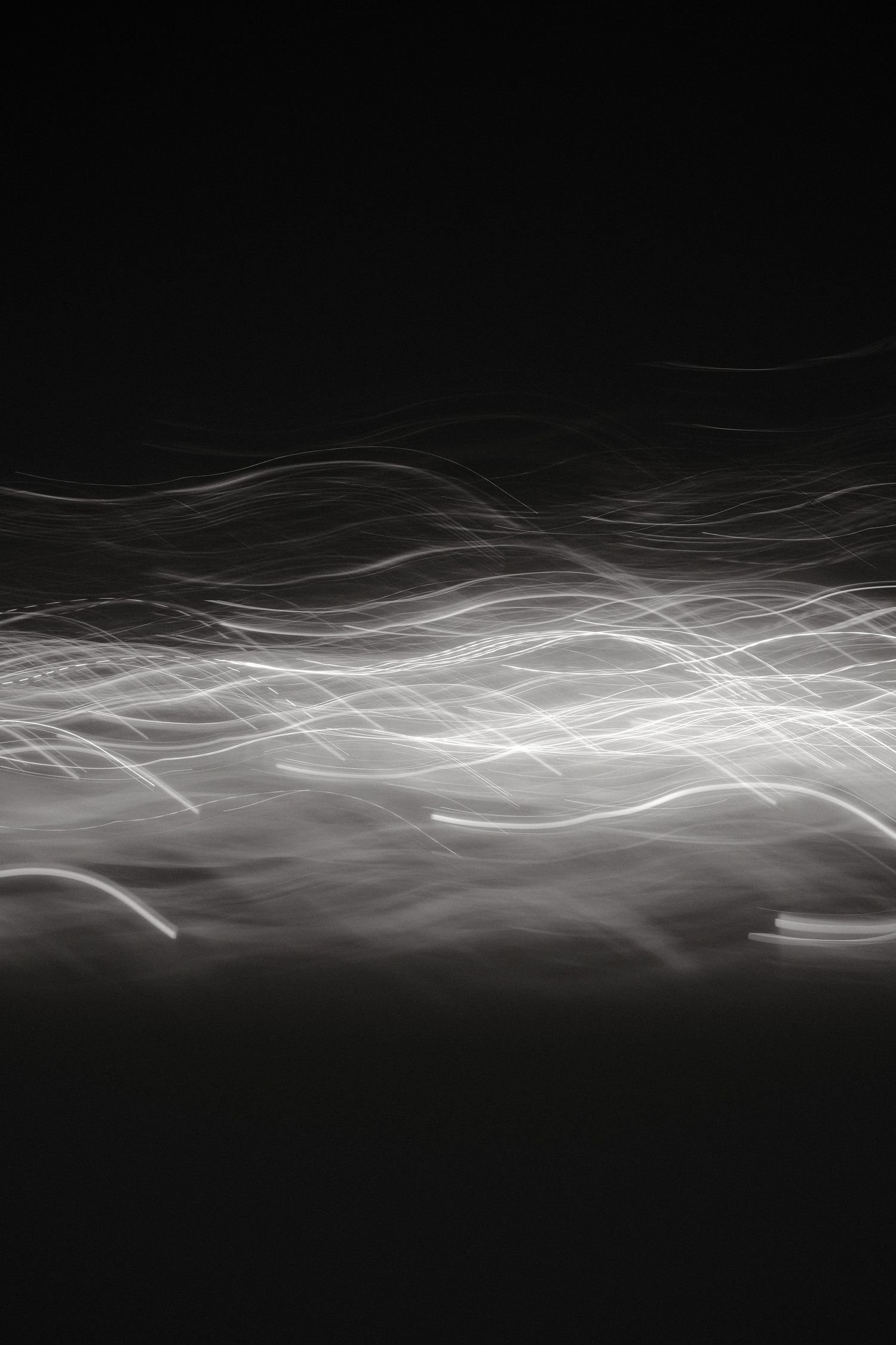 Abstract white light trails create flowing patterns against black background.