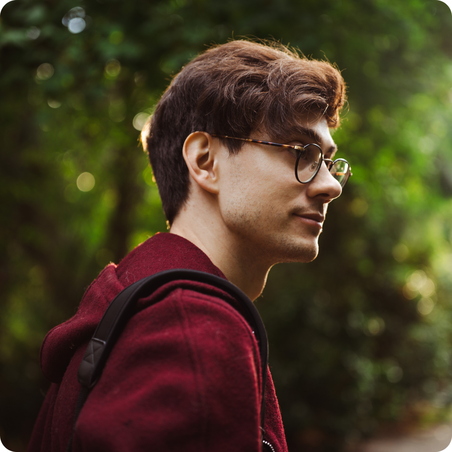 Person in burgundy hoodie photographed from behind in lush green forest setting.